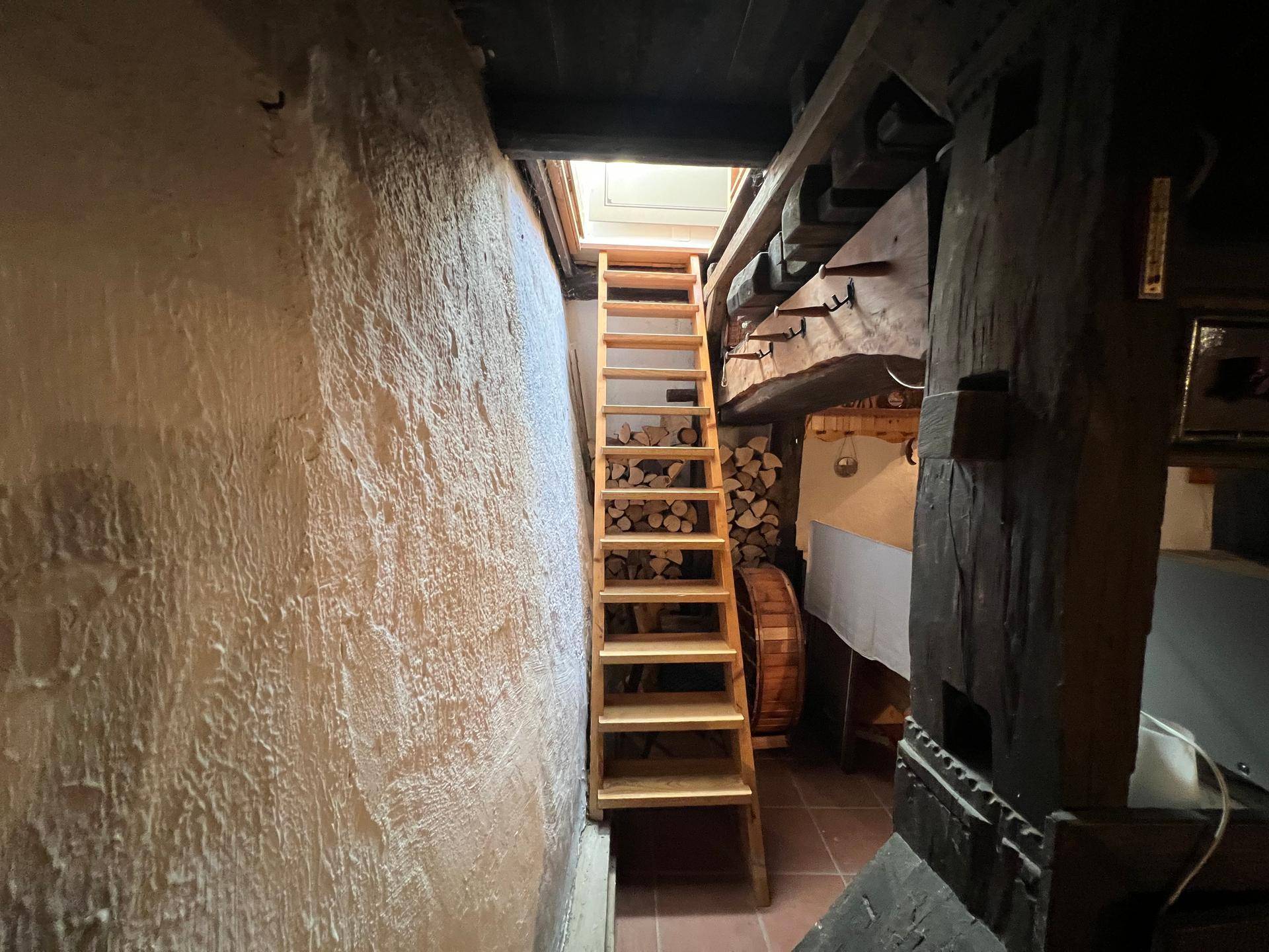 Steile Holztreppe führt zu einem oberen Bereich, beleuchtet durch ein Dachfenster.
