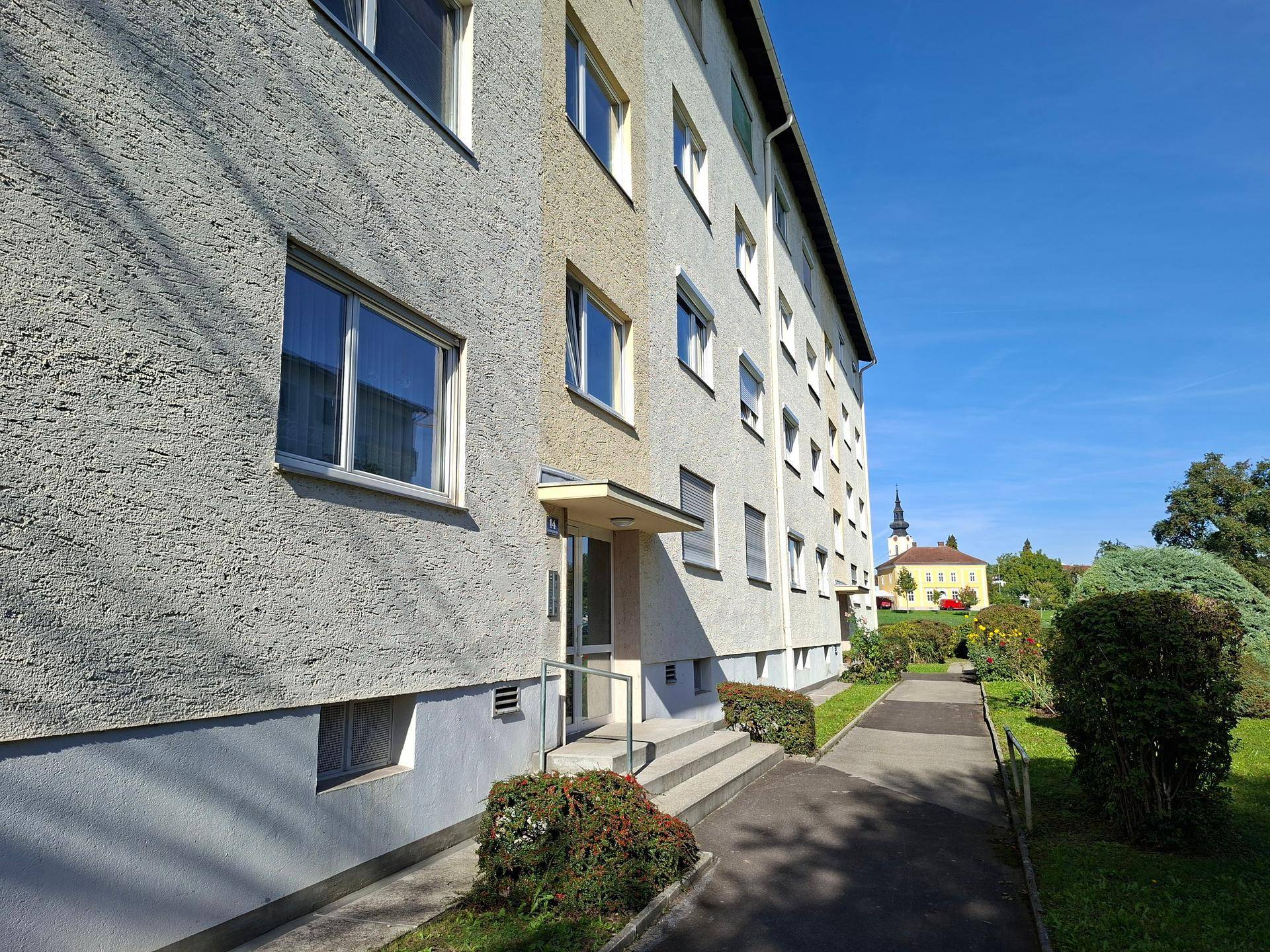 Mehrfamilienhaus mit gepflegter Fassade und Grünflächen im Außenbereich.