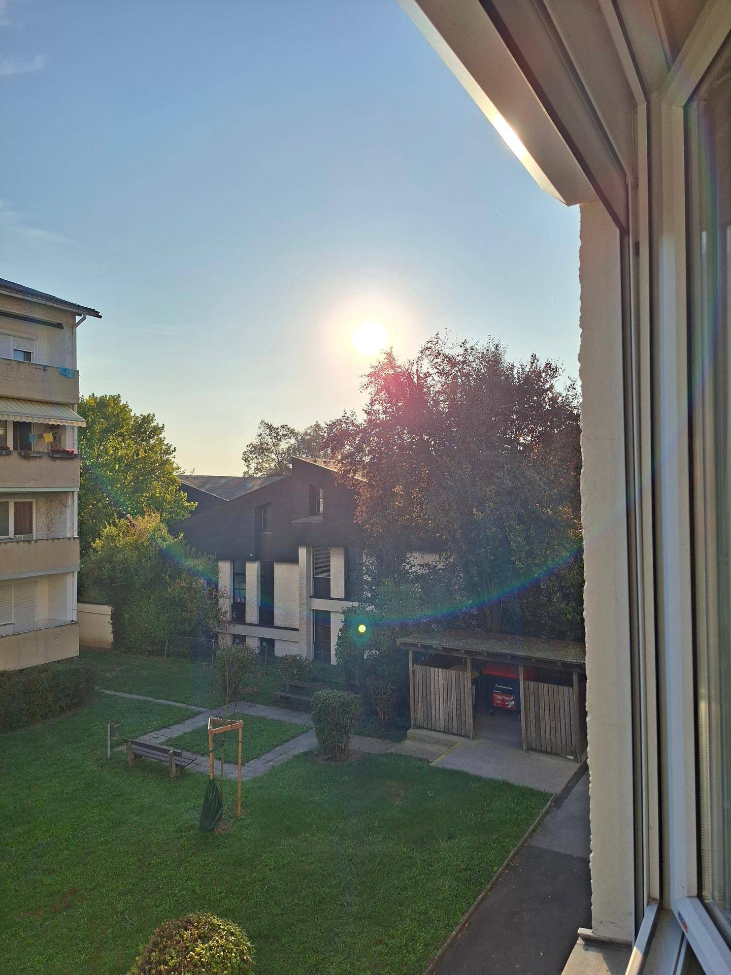 Blick aus dem Fenster auf den grünen Innenhof mit Spielplatz und Nebengebäuden.