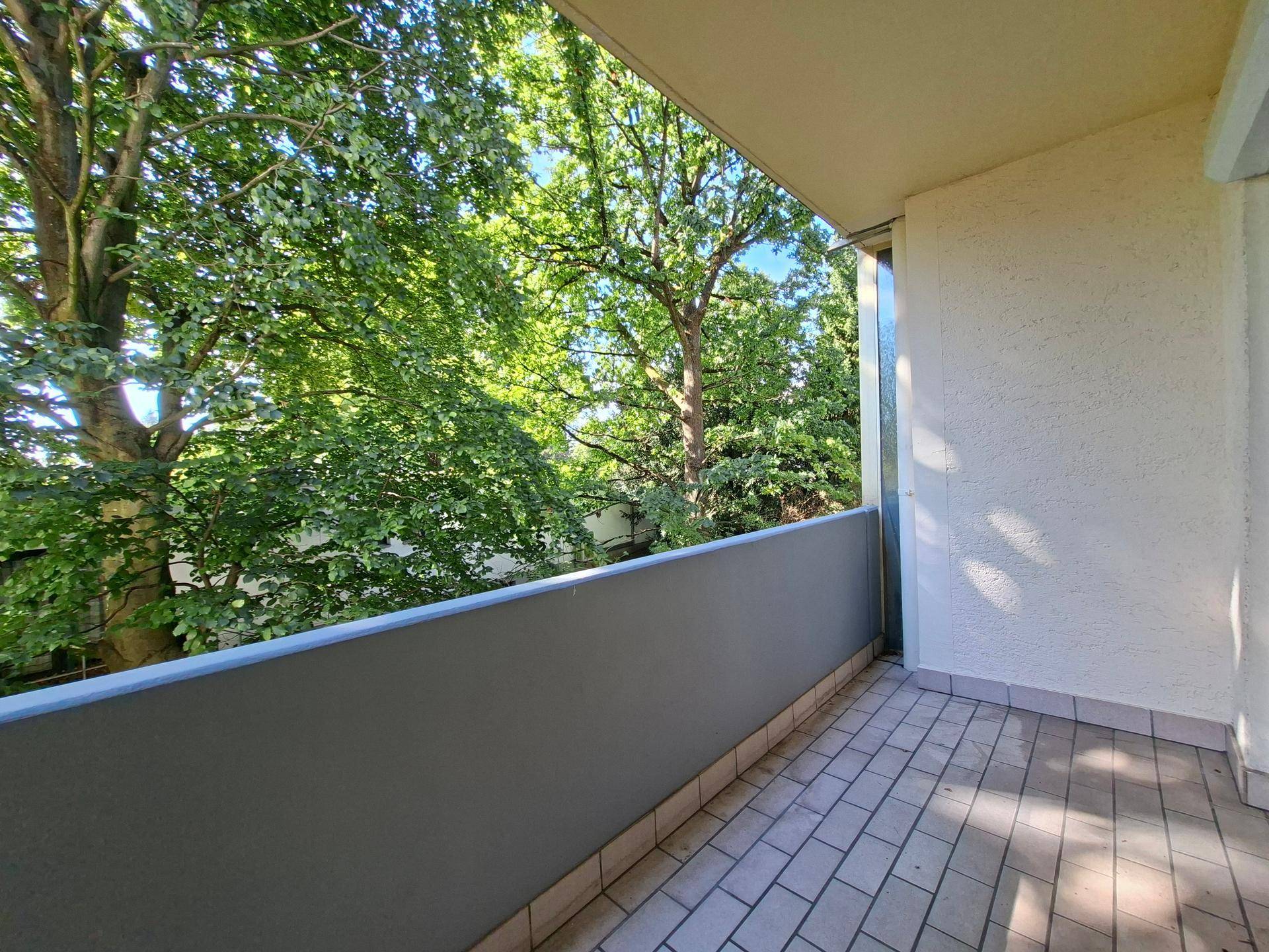 Sonniger Balkon mit Fliesenboden und Blick ins Grüne.