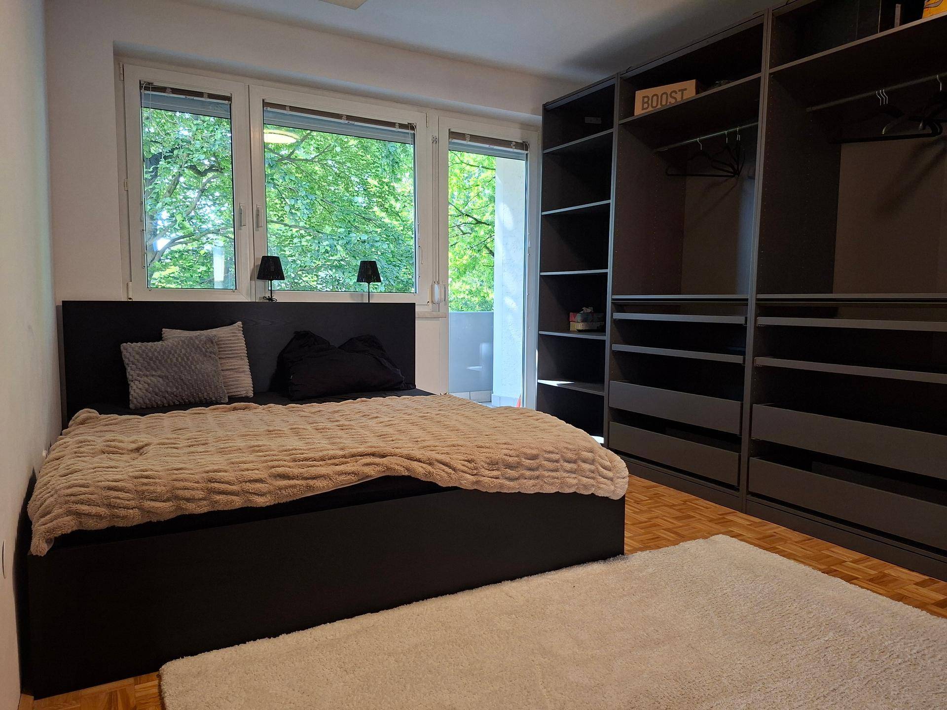 Helles Schlafzimmer mit großem Fenster, Doppelbett und geräumigem Einbauschrank.