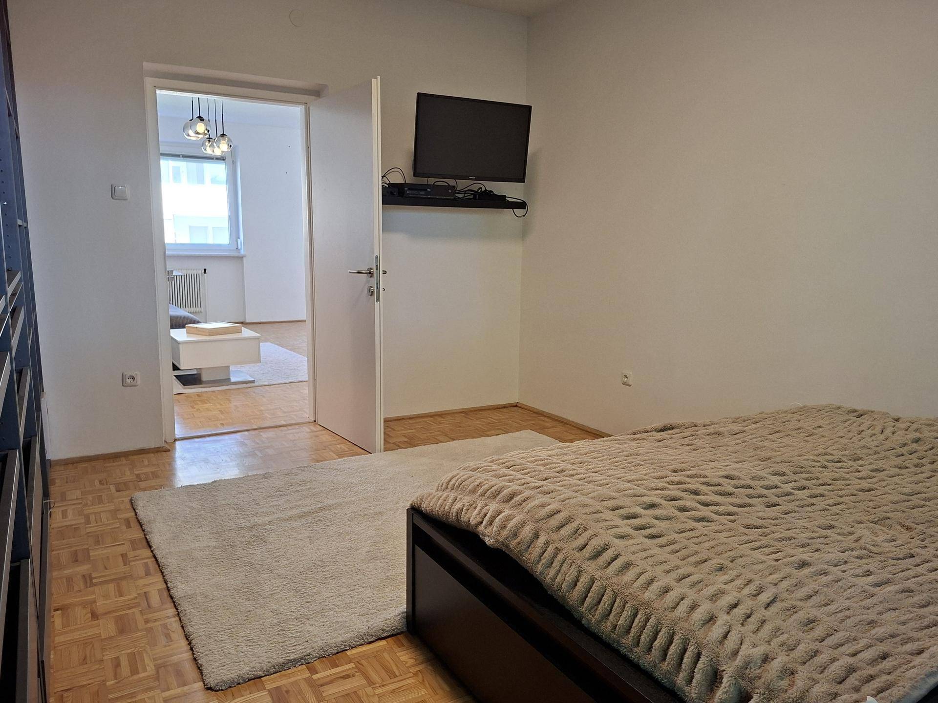 Schlafzimmer mit Doppelbett, Fernseher und Zugang zum Wohnbereich.