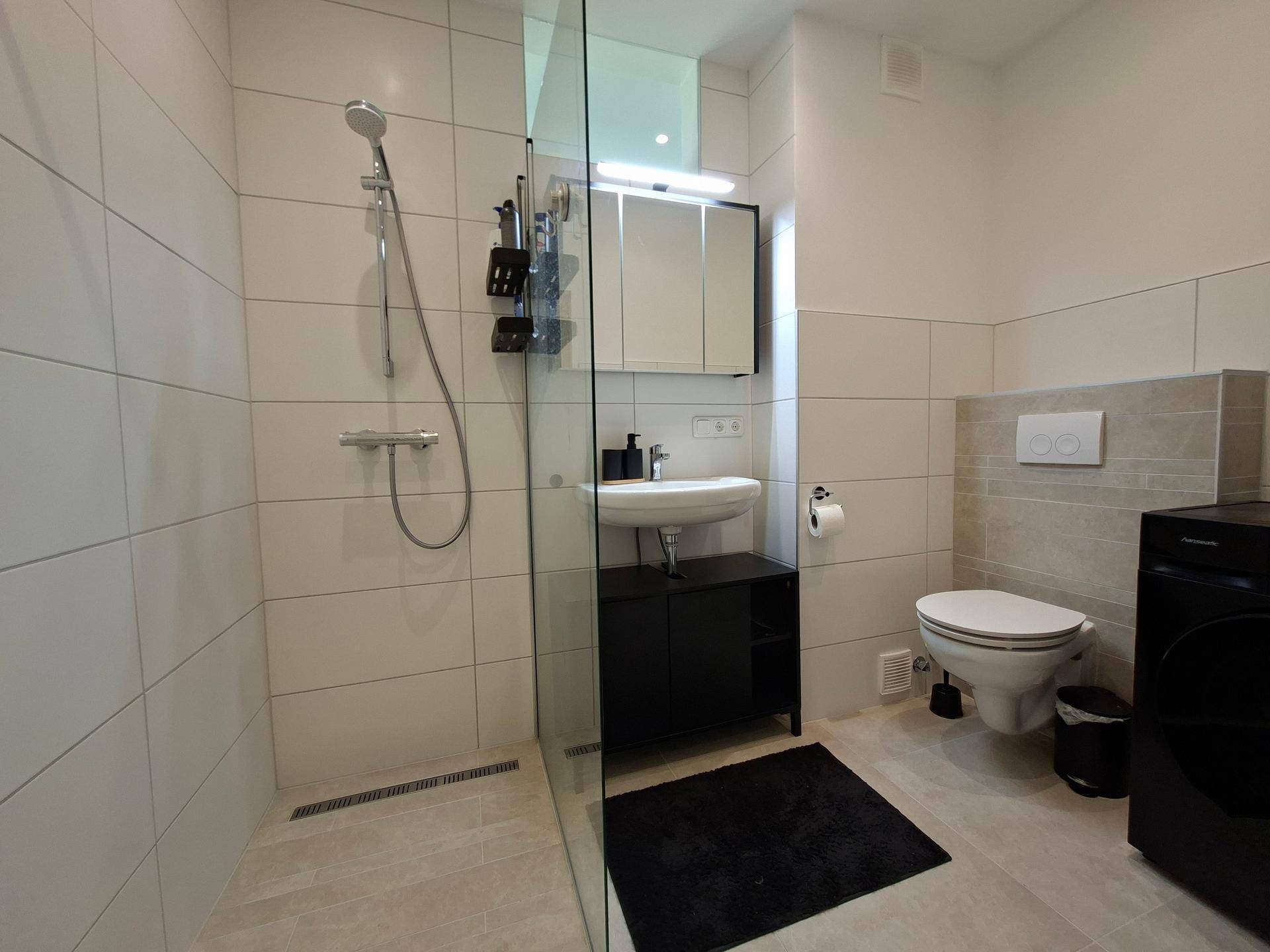Modernes Badezimmer mit ebenerdiger Dusche, WC und Waschbecken.