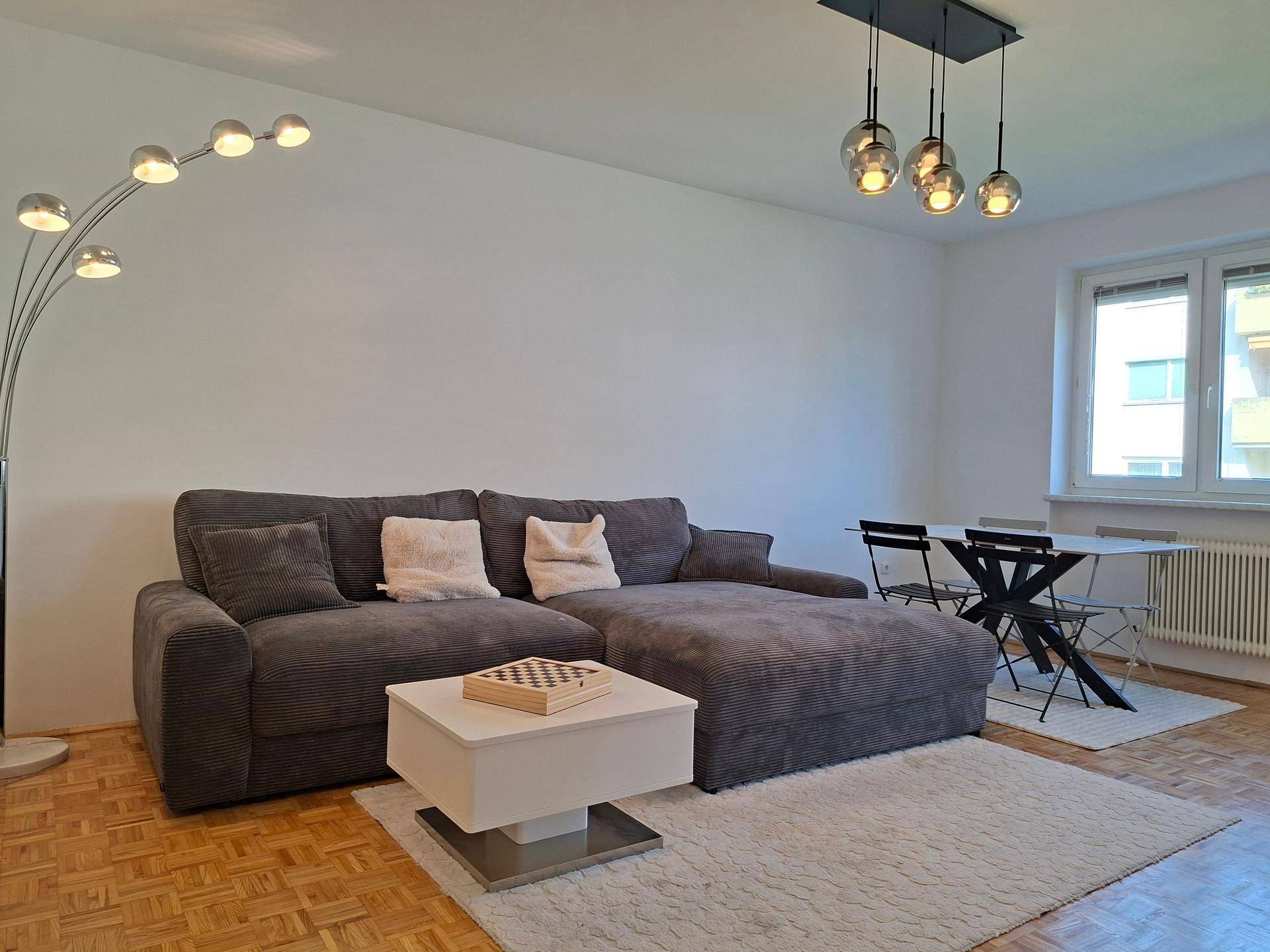 Heller Wohn- und Essbereich mit bequemer Couch, Esstisch und Parkettboden.