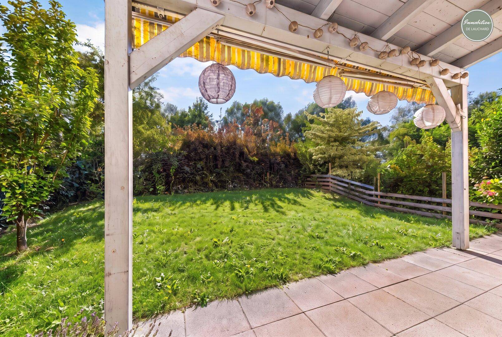 Überdachte Terrasse mit Gartenblick, umgeben von Grün und Pflanzen.