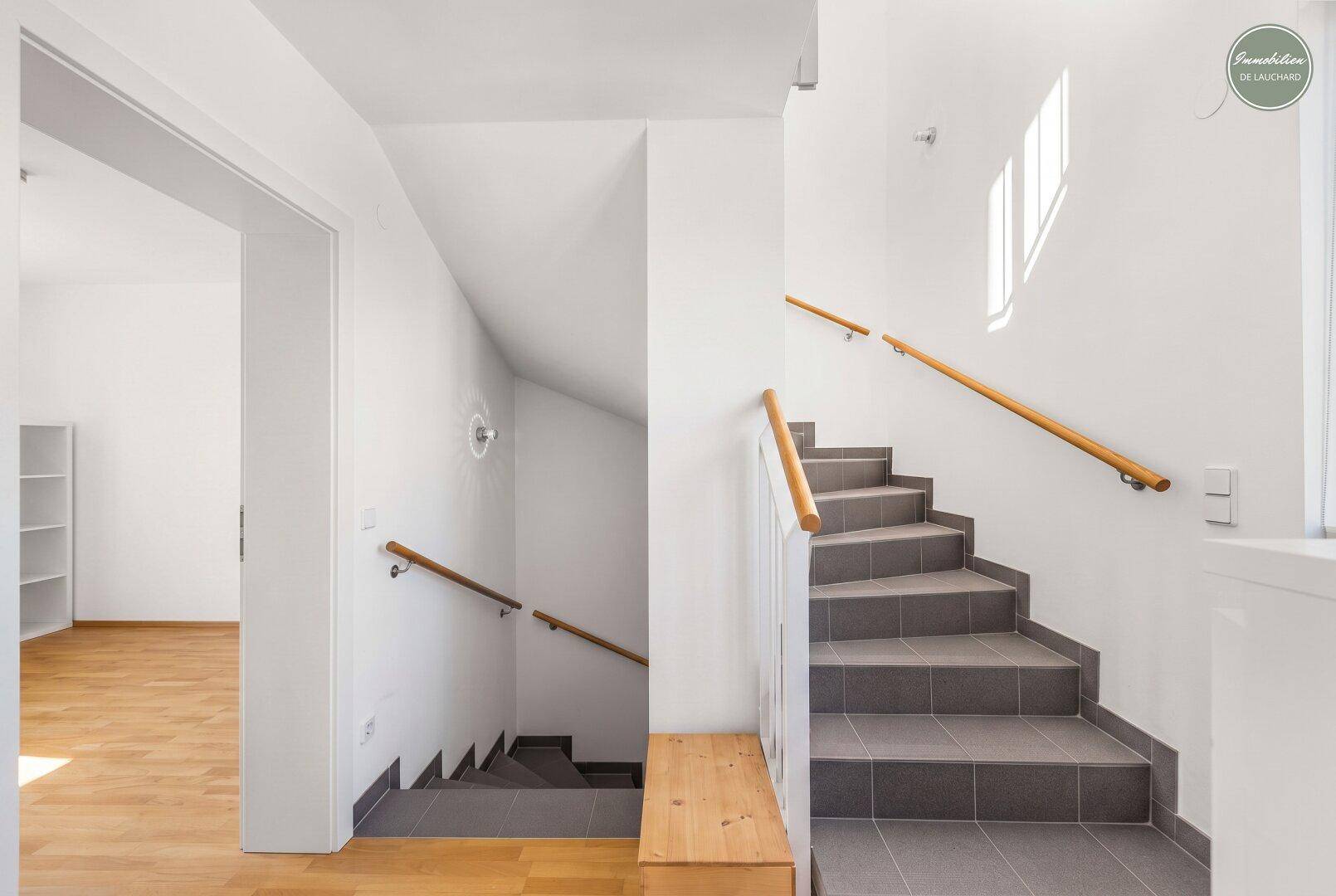 Treppenhaus mit Fliesenstufen, Holzgeländer und hellem Anstrich.