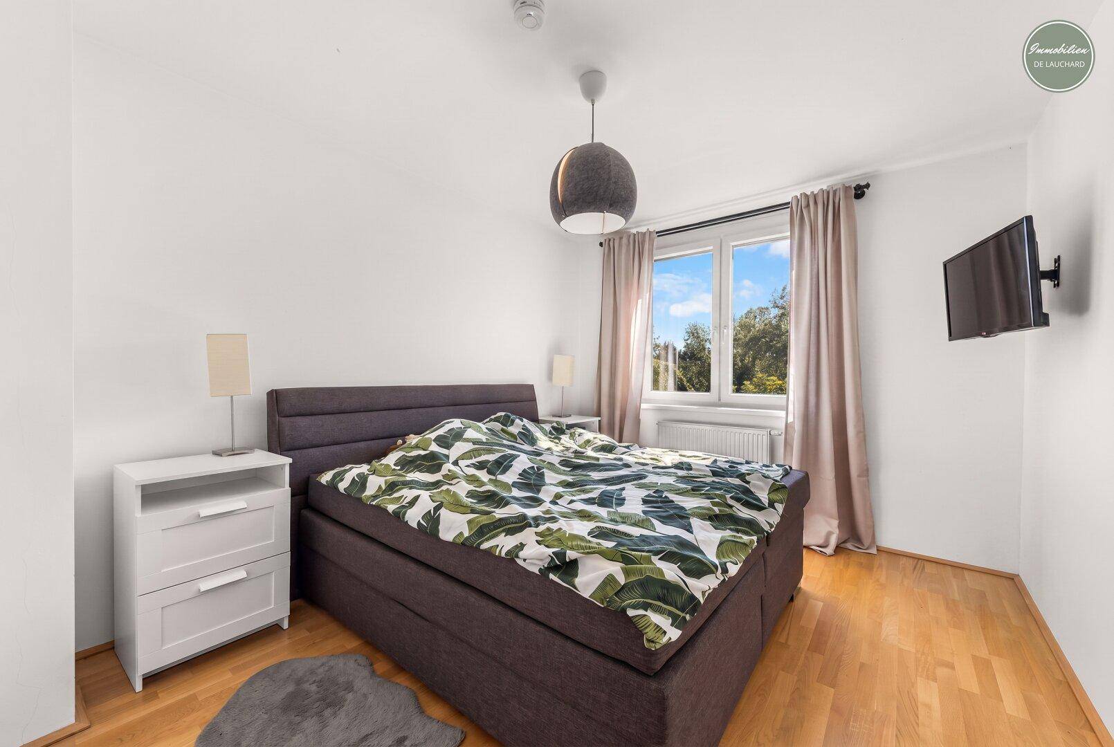 Gemütliches Schlafzimmer mit Doppelbett, Holzboden und Blick ins Grüne.