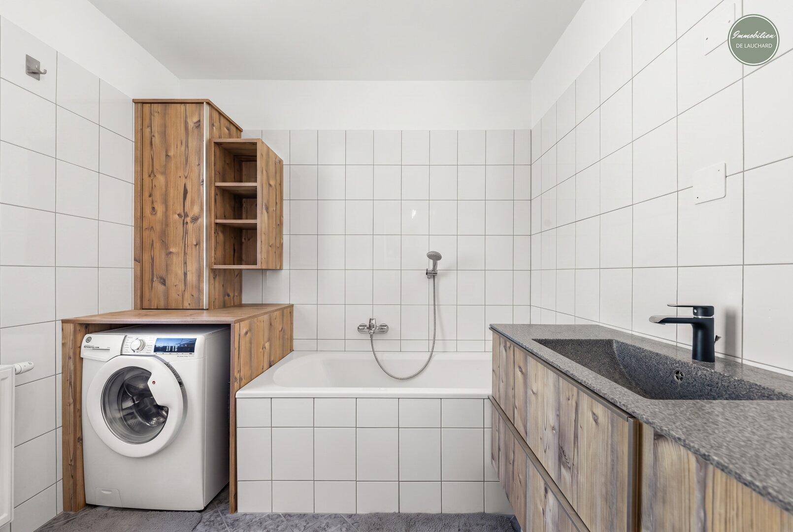 Badezimmer mit Badewanne, Waschmaschine und Holzmöbeln im Landhausstil.