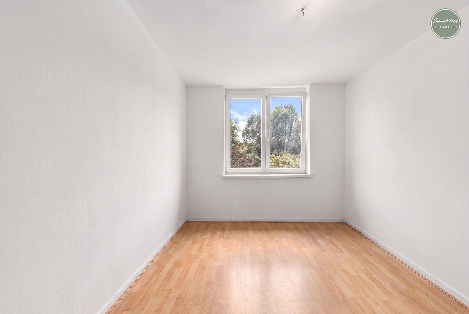 Helles Zimmer mit Holzboden und Fenster mit Blick ins Grüne.