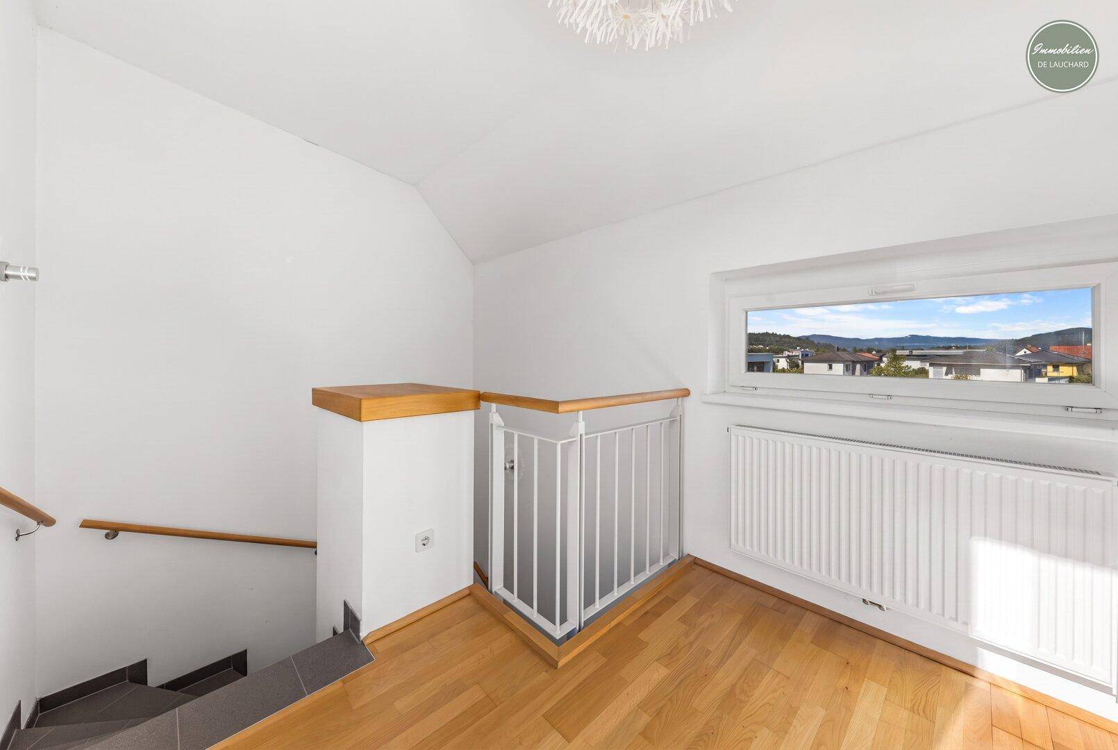 Heller Treppenabsatz mit Holzboden, Geländer und Fenster mit Ausblick.