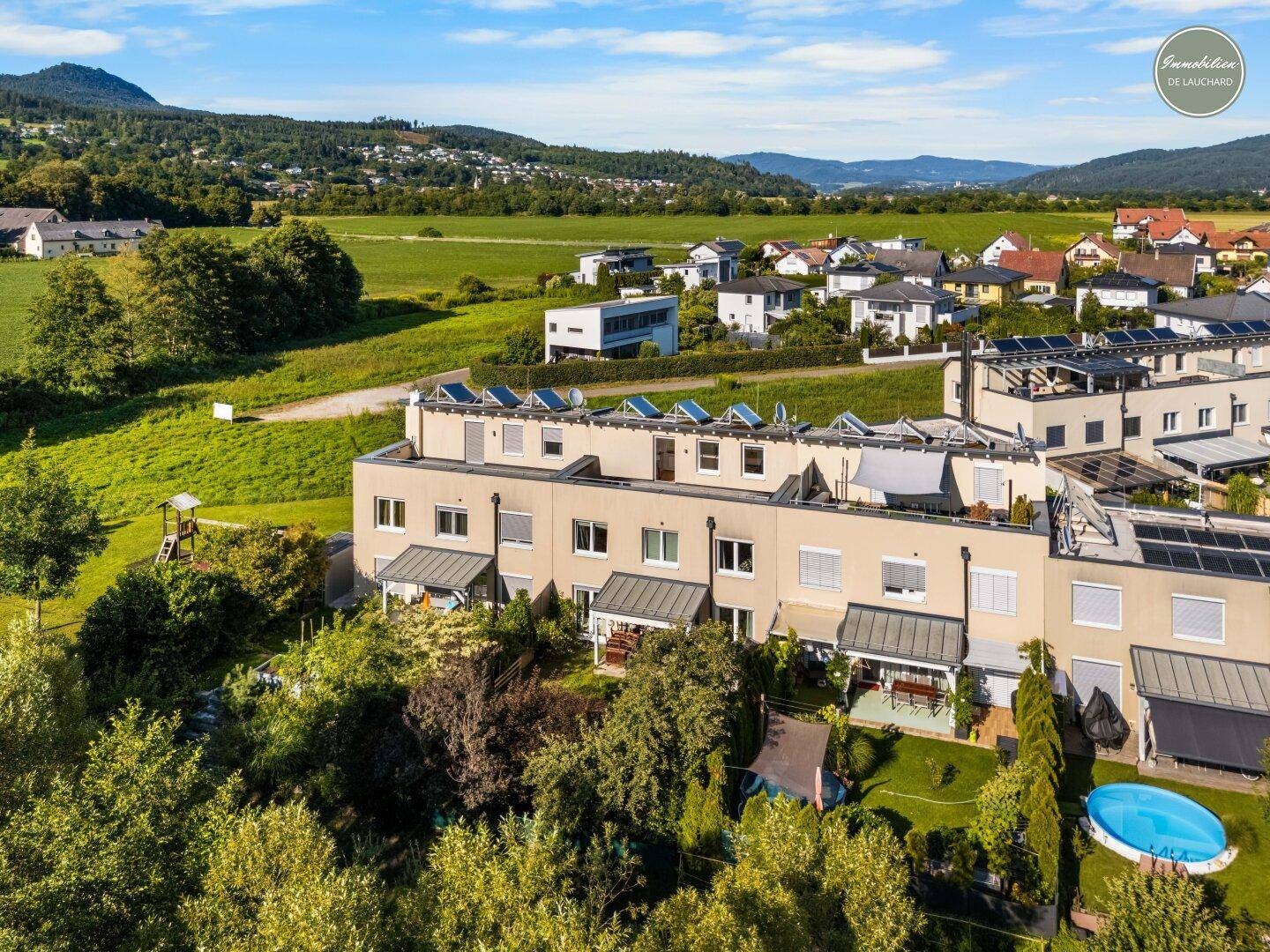 Luftaufnahme einer modernen Reihenhaussiedlung mit Gärten und Blick auf die umliegende Landschaft.