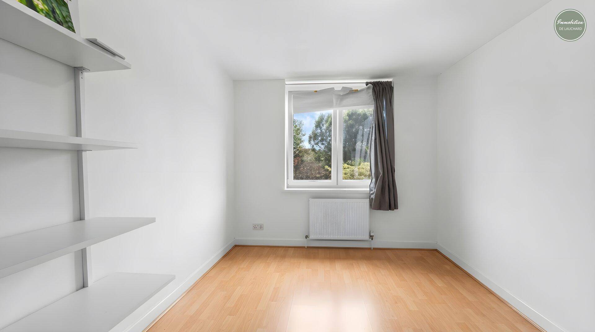 Leeres Zimmer mit Holzboden, Regal und Fenster mit Blick nach draußen.