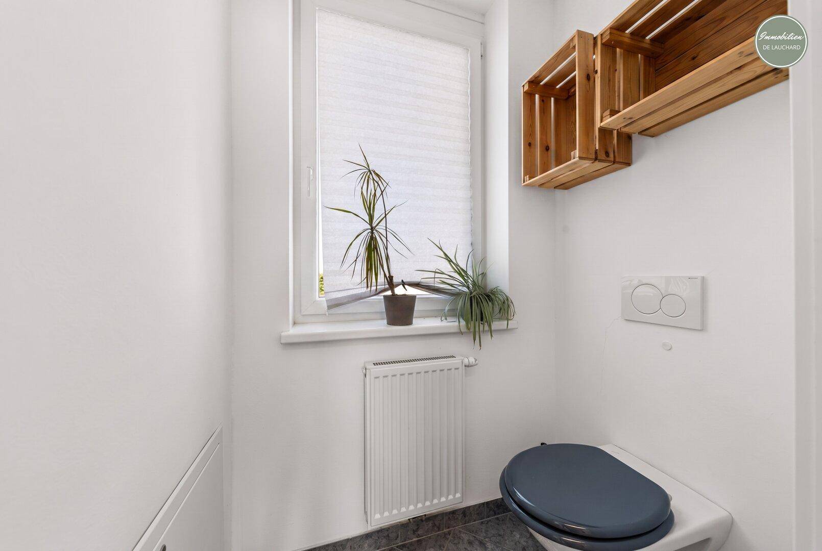 Modernes Gäste-WC mit Fenster, wandhängendem WC und dekorativen Holzkisten.