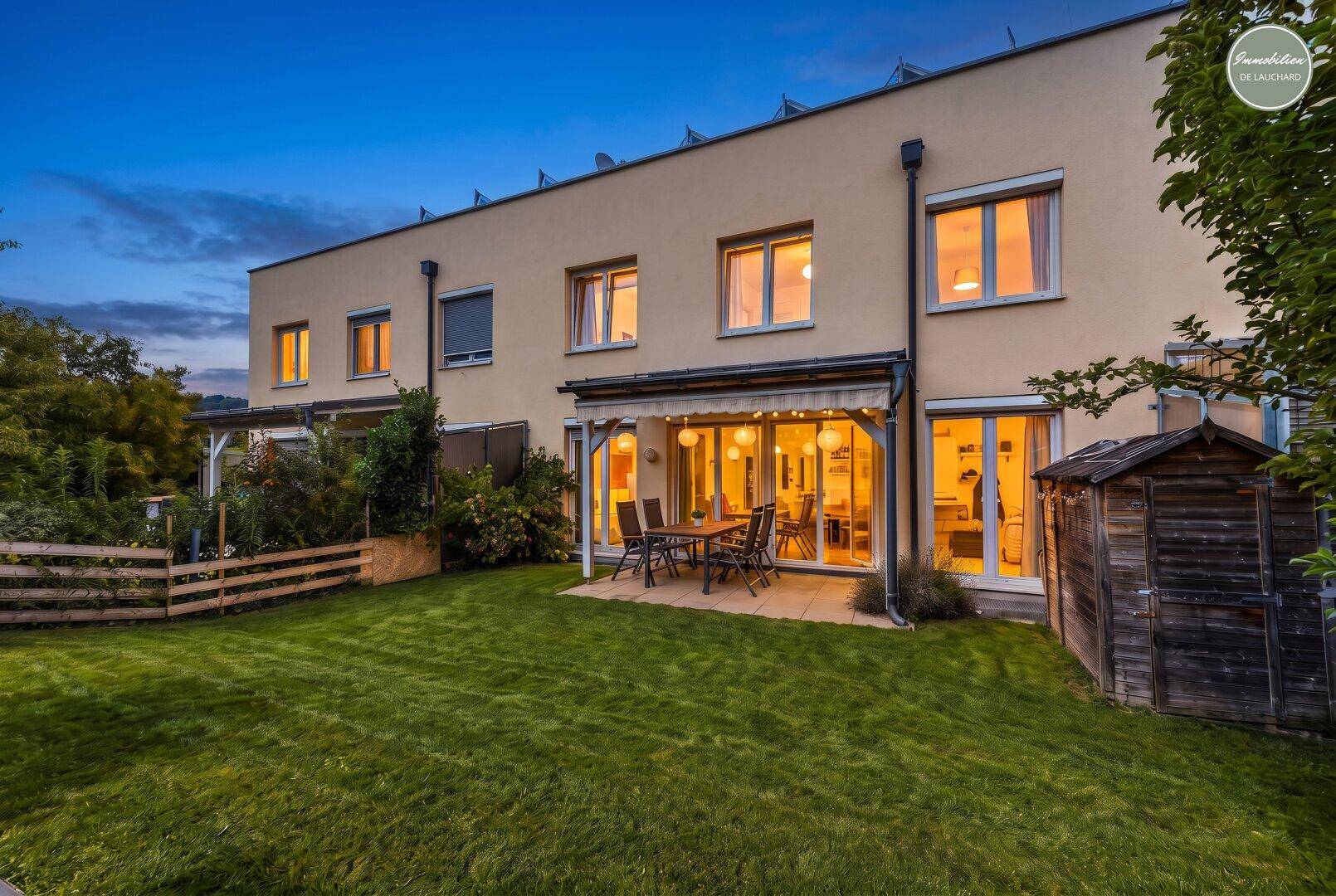 Reihenhausfassade am Abend mit beleuchteter Terrasse und Gartenbereich.