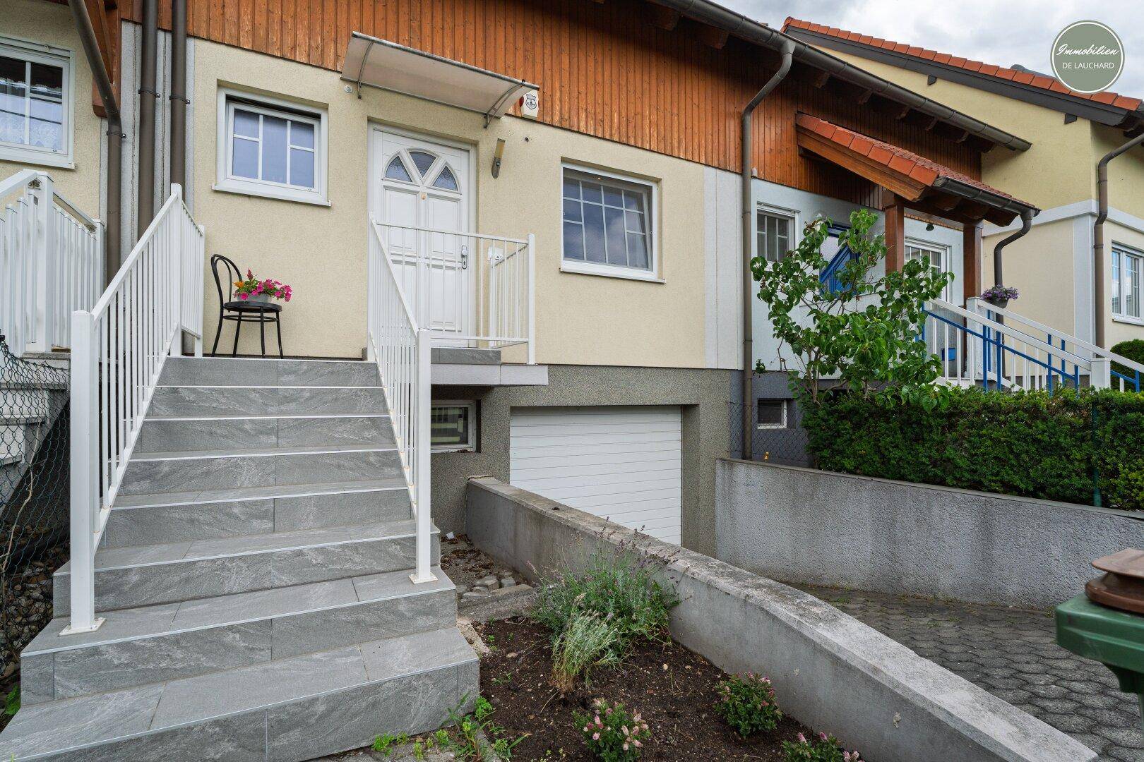 Vorderansicht des Hauses mit Eingangsbereich, Treppe und Garagenzufahrt.