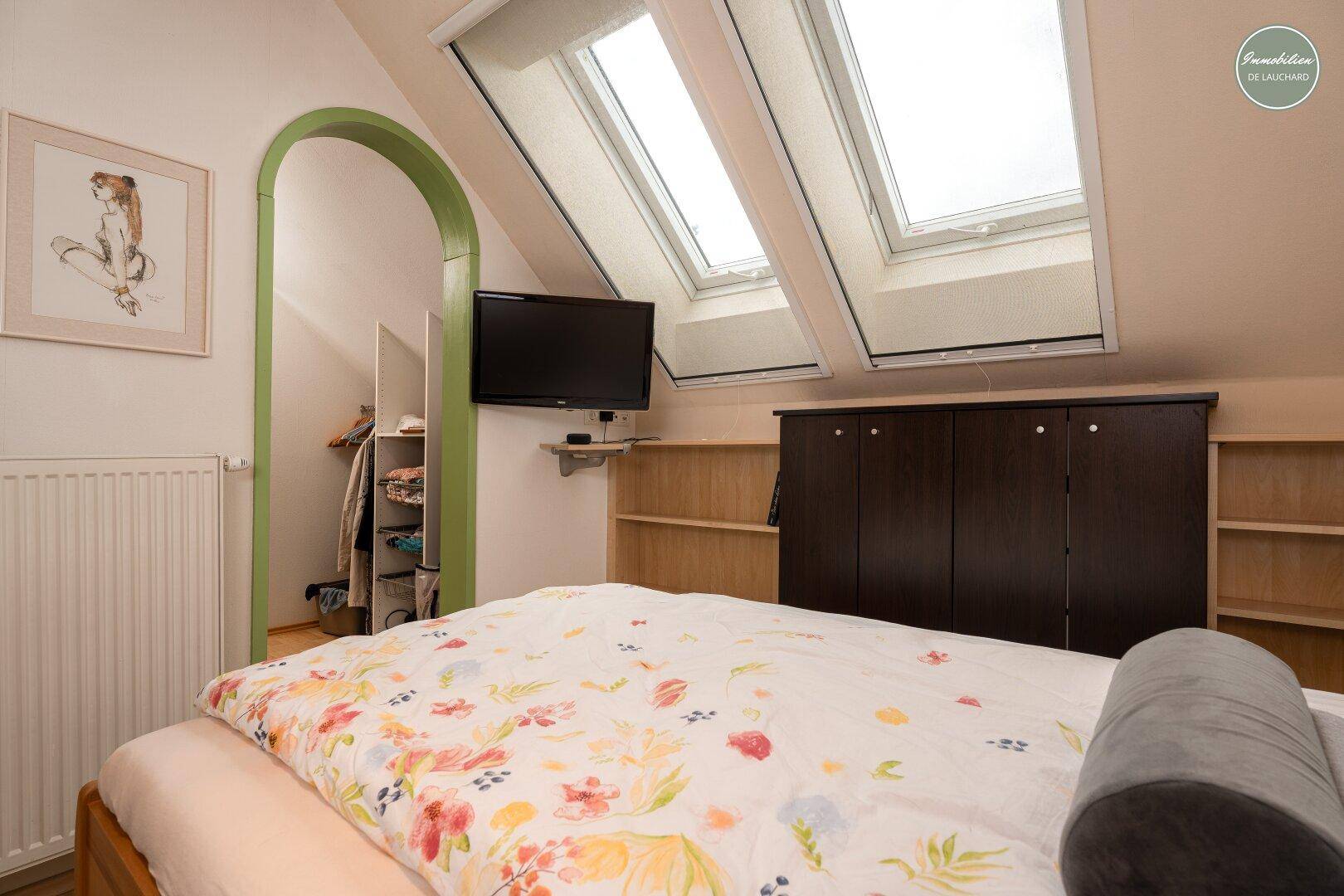 Schlafzimmer mit Doppelbett, Fernseher und offenem Zugang zum begehbaren Kleiderschrank.