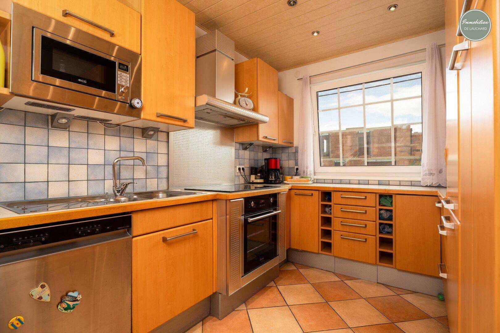 Funktionale Küche mit Holzschränken, Edelstahlgeräten und Fensterblick.