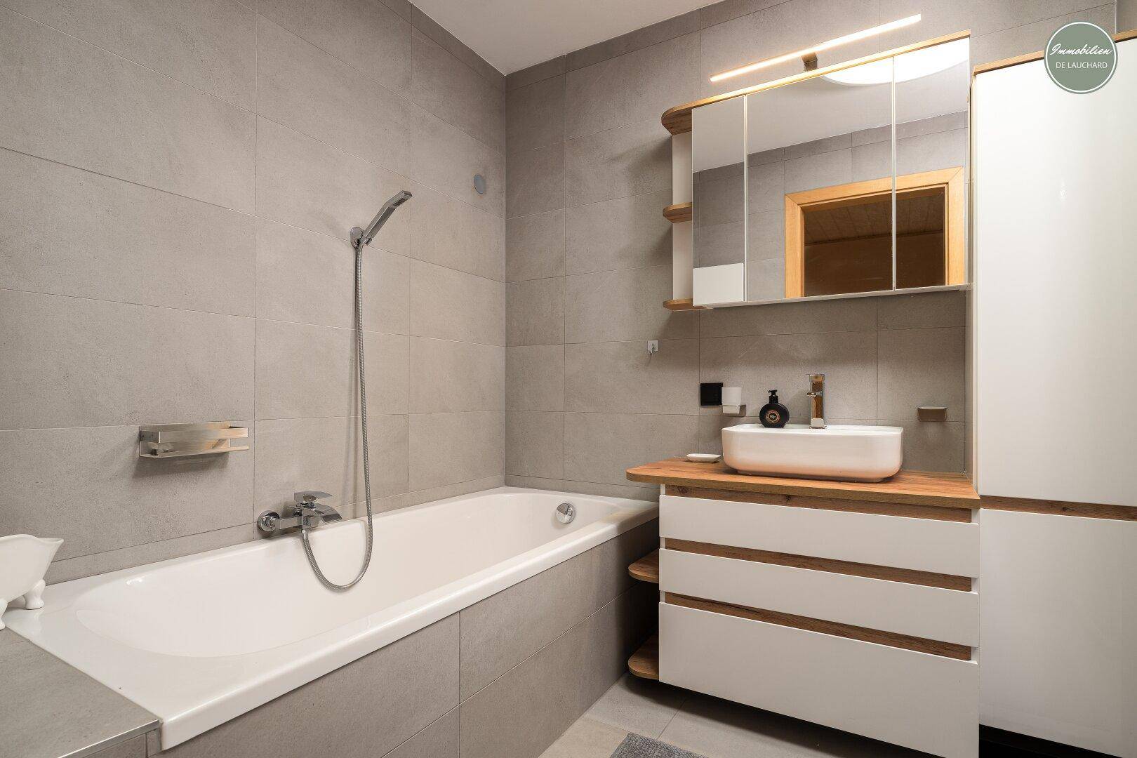 Modernes Badezimmer mit Badewanne, Einzelwaschbecken und grauen Fliesen.