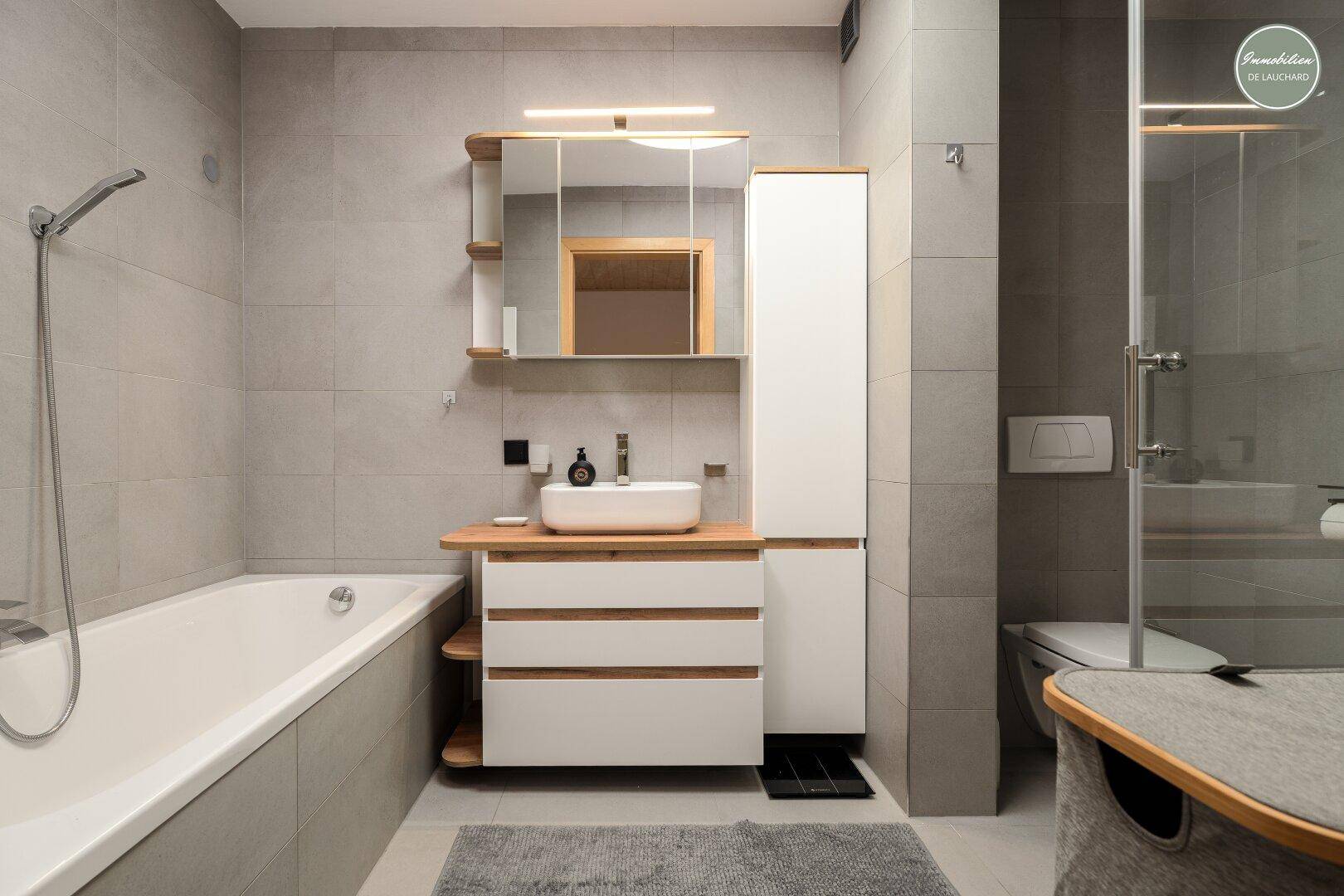 Helles Badezimmer mit Badewanne, Dusche, WC und modernem Waschtisch.
