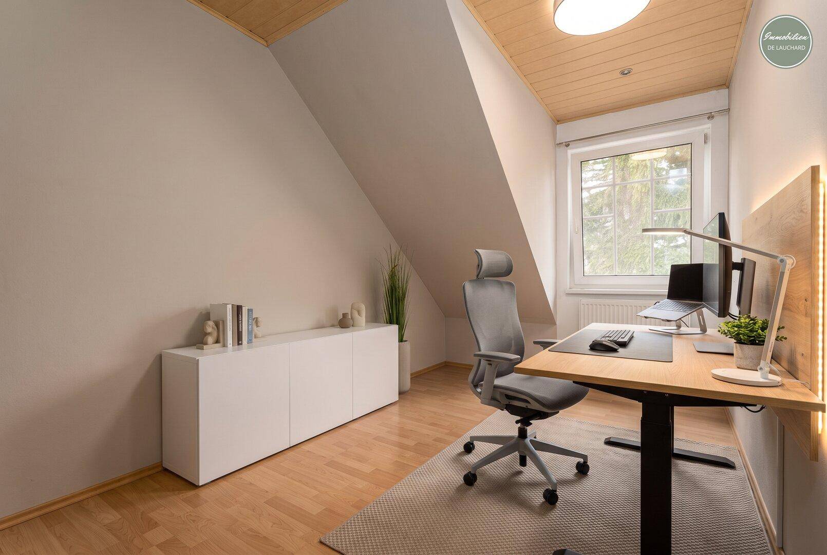 Helles Arbeitszimmer im Dachgeschoss mit Schreibtisch, Bürostuhl und Holzdecke.