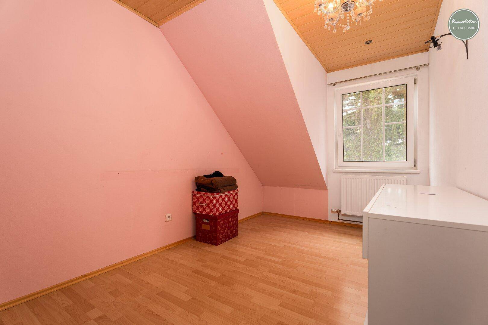 Leeres Zimmer mit rosa Wänden, Laminatboden und Dachschräge.