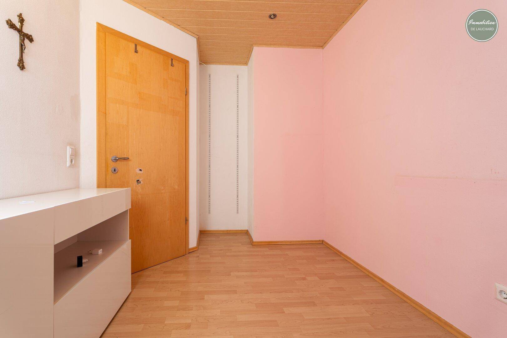 Zimmer mit rosa Wänden, Holztür und Laminatboden im Dachgeschoss.