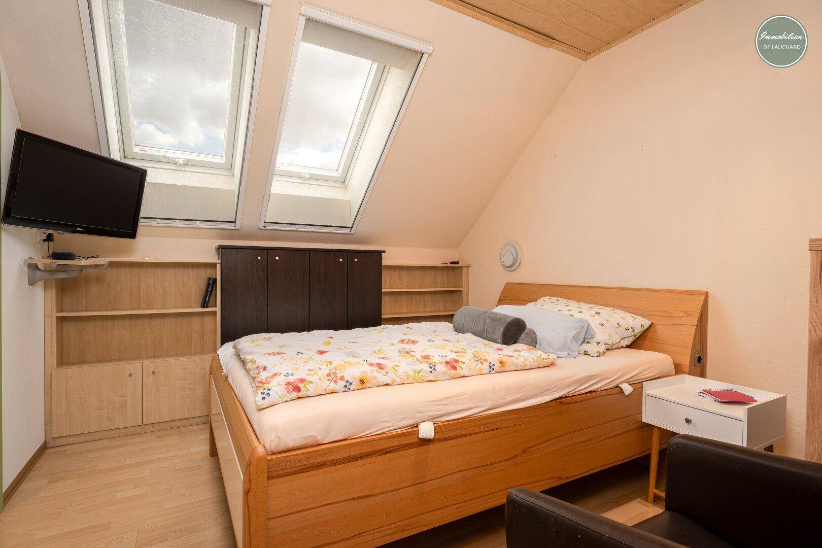 Gemütliches Schlafzimmer mit Doppelbett, Fernseher und zwei Dachfenstern.