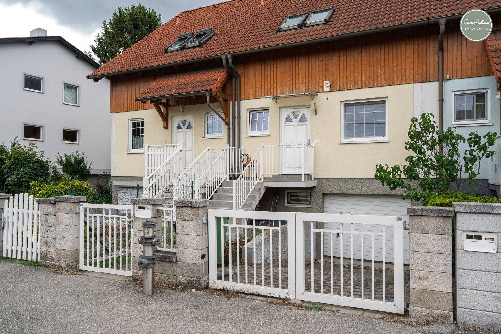 Reihenhausfassade mit rotem Ziegeldach, weißen Toren und Eingangsbereichen in einer Wohnsiedlung.