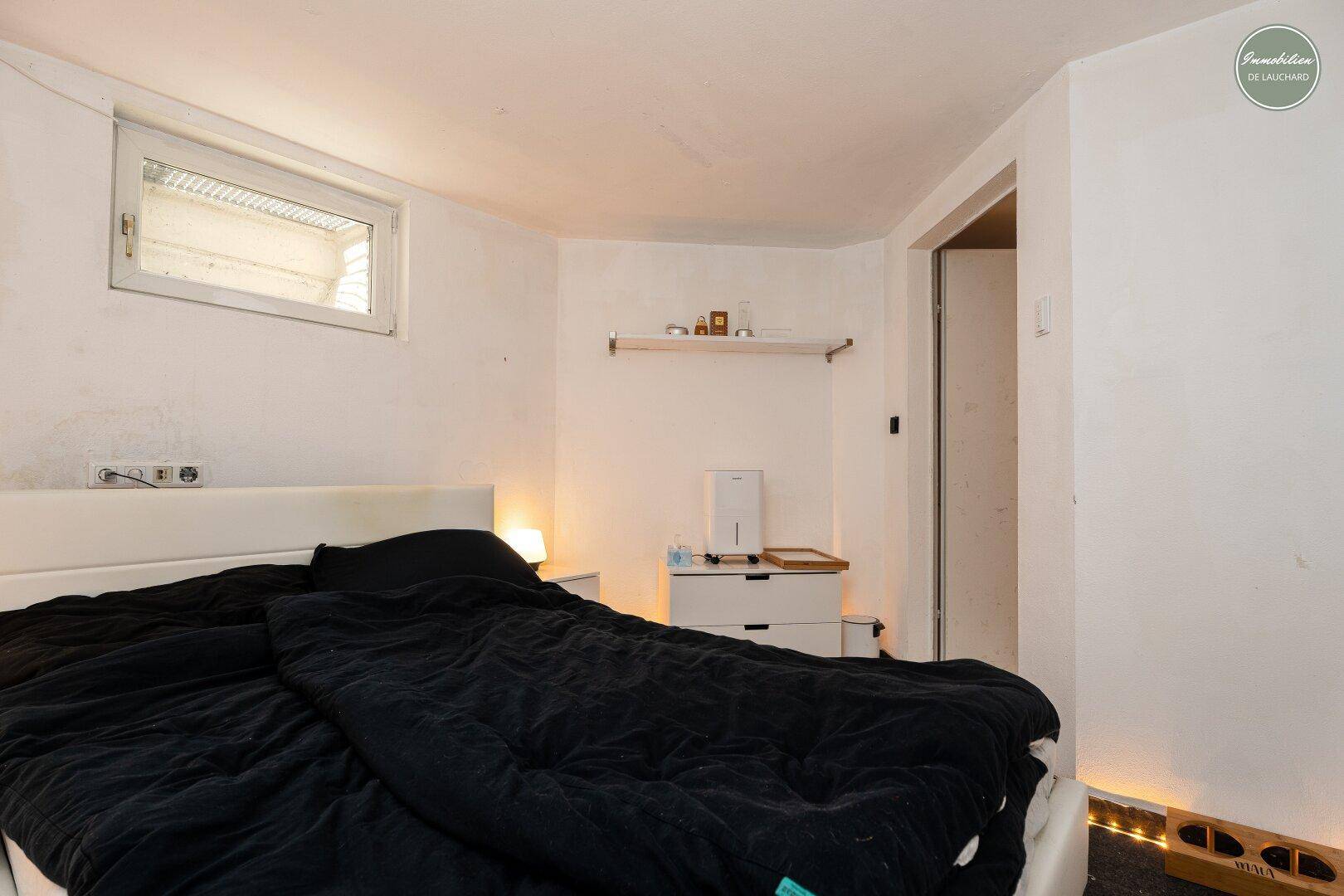 Einfaches Schlafzimmer im Untergeschoss mit minimalistischer Einrichtung und indirekter Beleuchtung am Boden.