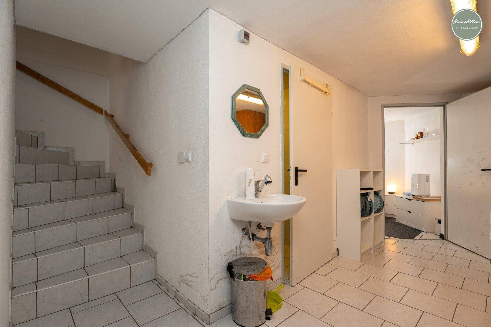Flur mit gefliestem Boden, Treppe ins Obergeschoss und kleinem Waschbecken an der Wand.