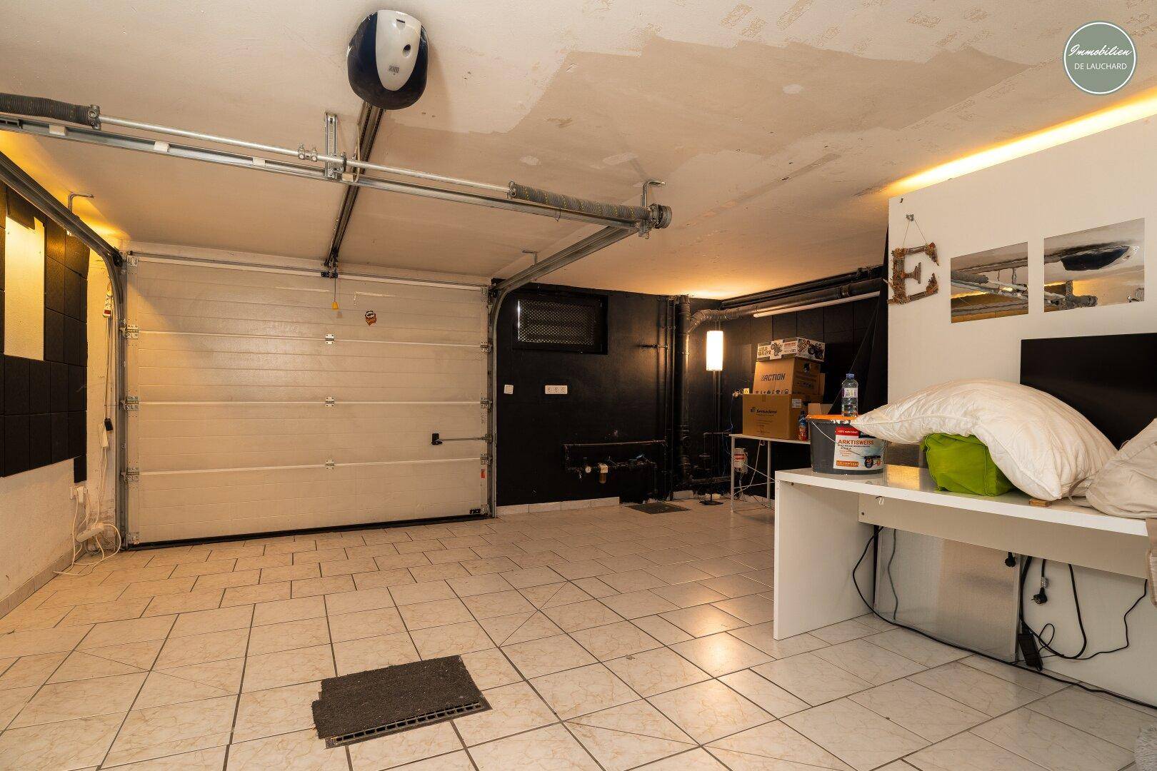Geräumige Garage mit Fliesenboden, Garagentor und indirekter Beleuchtung entlang der Wände.