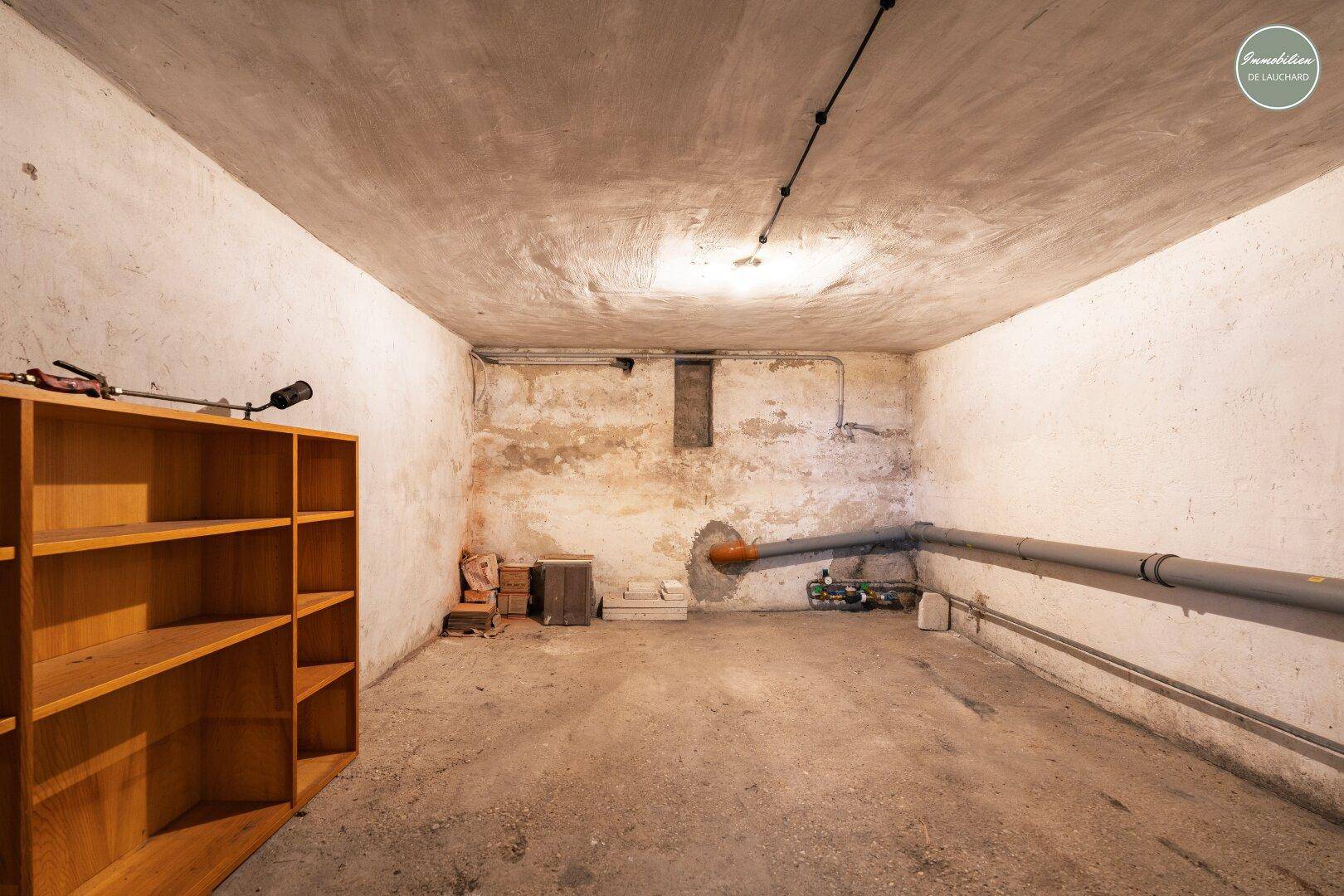 Einfacher Kellerraum mit Betonwänden und einem Holzregal, ideal für zusätzlichen Stauraum.