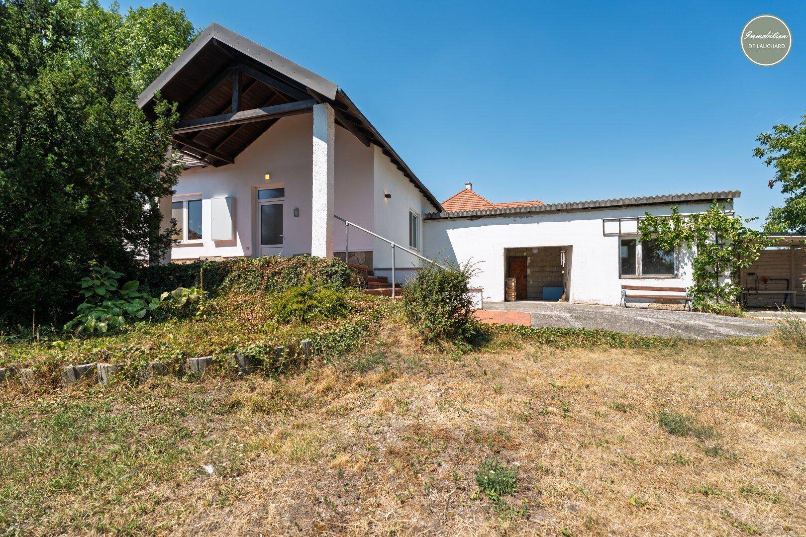 Einfamilienhaus mit weißer Fassade, Satteldach und angrenzender Garage unter klarem Himmel.