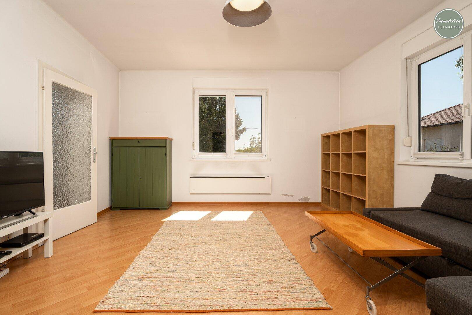 Heller Wohnbereich mit Holzboden, großen Fenstern und viel Tageslicht, ideal zum Entspannen.