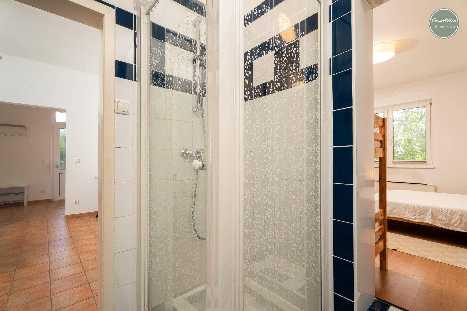 Duschbereich im Badezimmer mit Glasabtrennung und Blick auf den angrenzenden Flur.