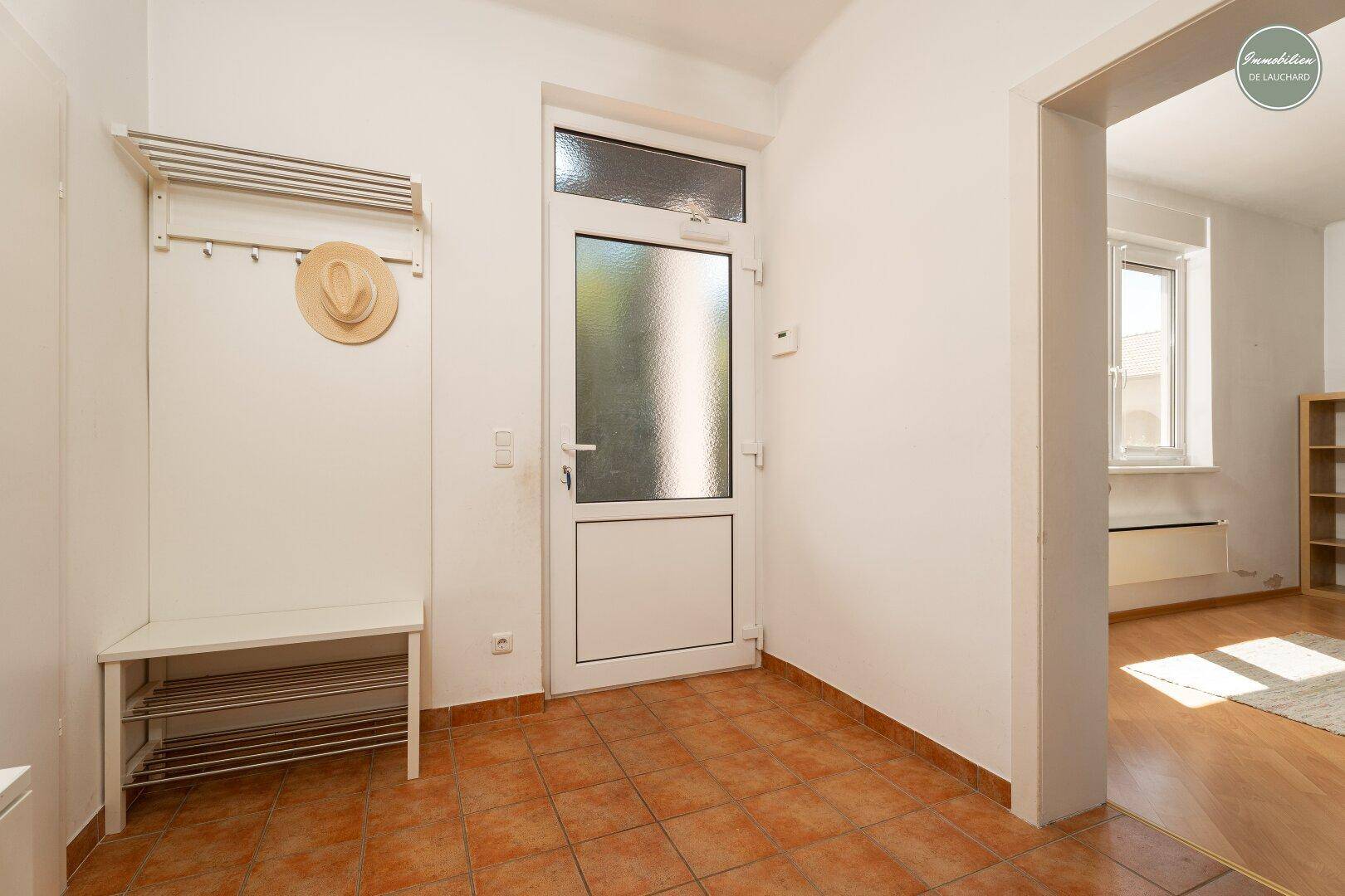 Heller Eingangsbereich mit Terrakottafliesen, Garderobe und Zugang zu weiteren Räumen.