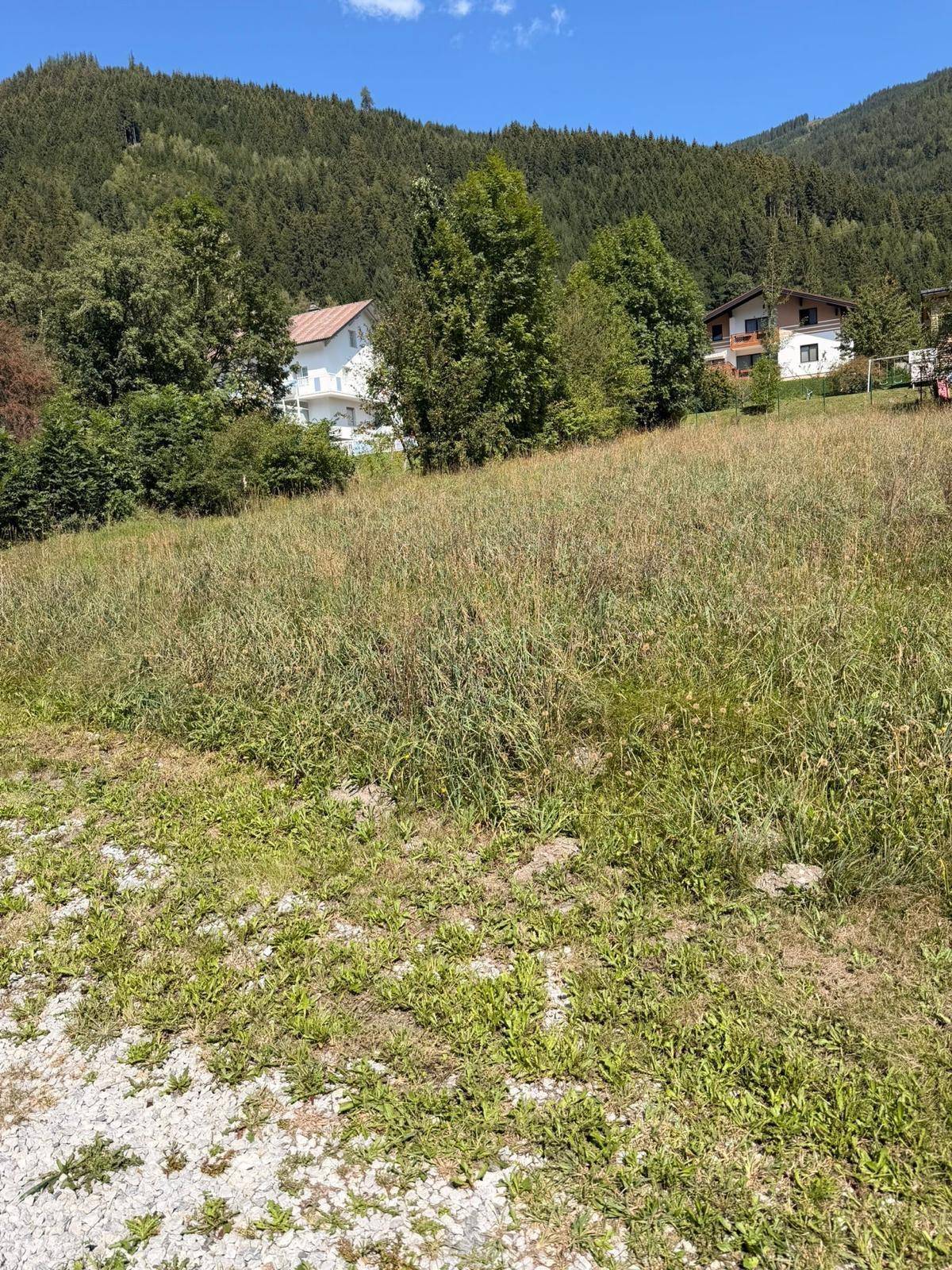 Grünes Grundstück mit Blick auf die umliegende Natur und Wohnhäuser am Fuße des Berges.