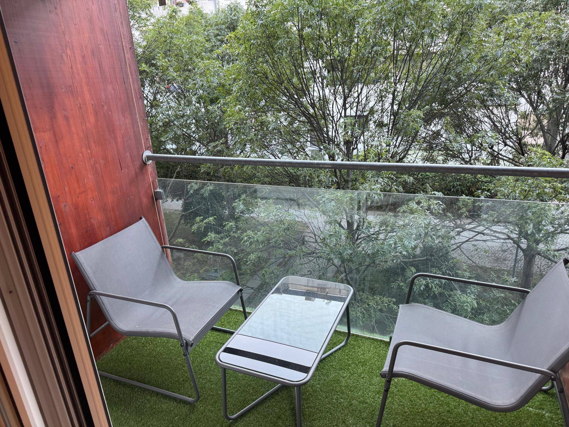 Gemütlicher Balkon mit kleinem Tisch und Stühlen, umgeben von Bäumen.