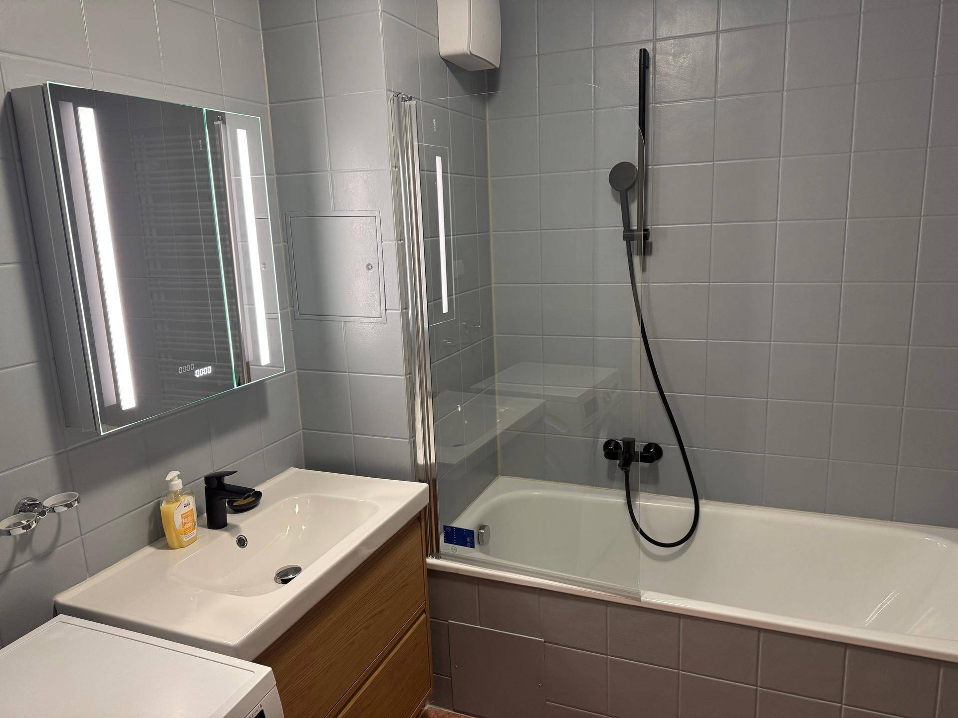 Modernes Badezimmer mit Badewanne, Duschabtrennung und beleuchtetem Spiegelschrank.