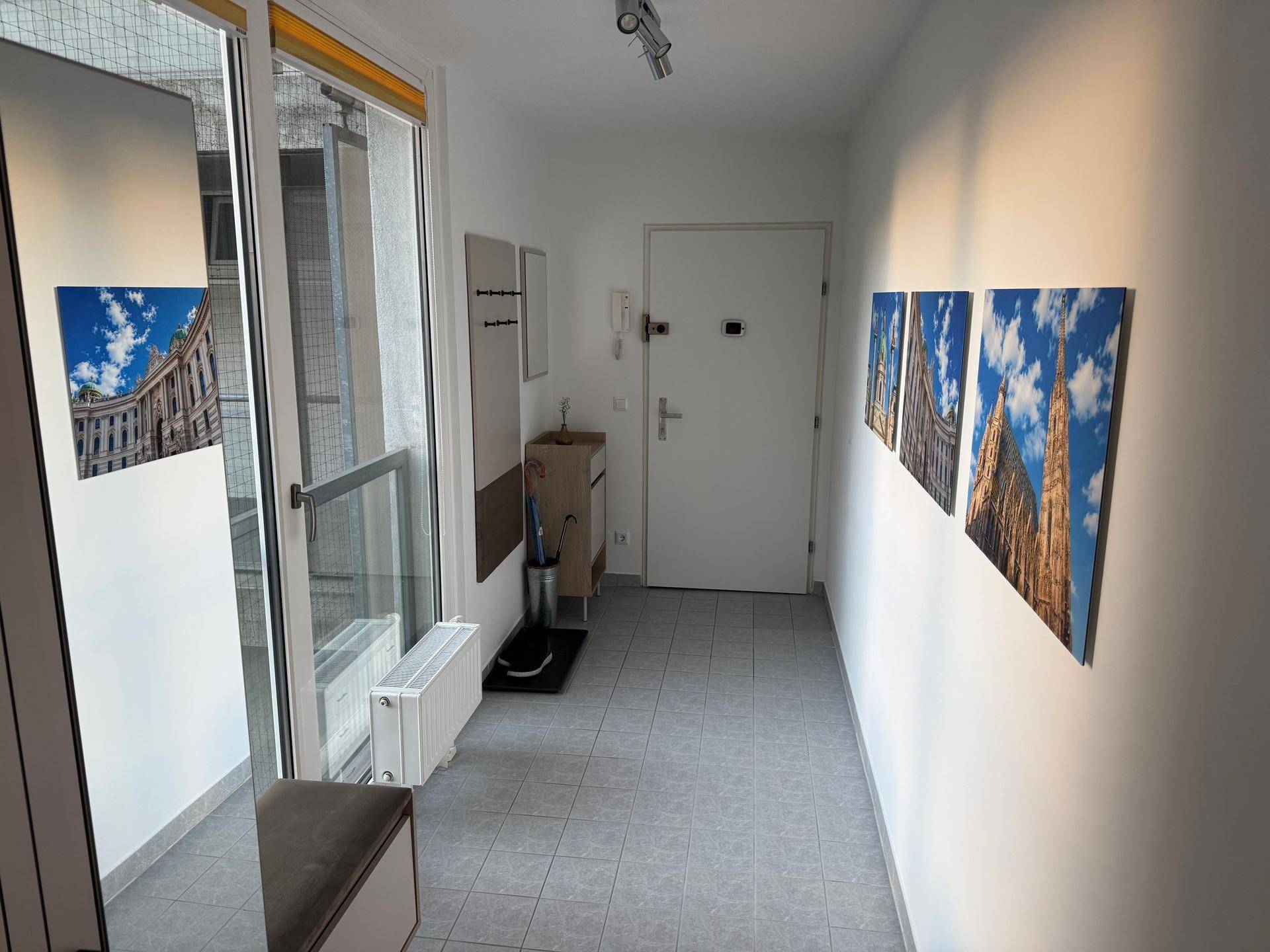 Heller Flur mit Fliesenboden, Garderobe und Zugang zum Balkon.
