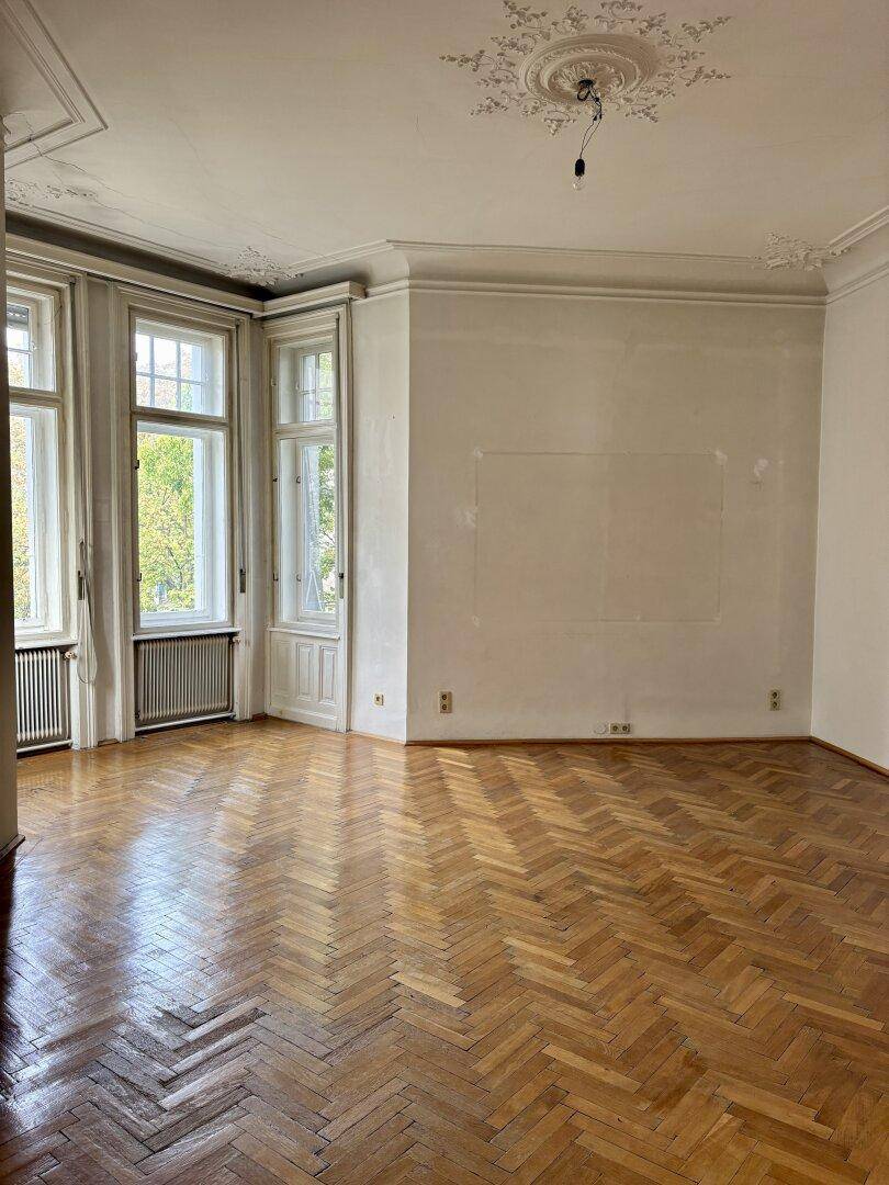 Helles Wohnzimmer mit Fischgrätparkett, hohen Decken und Stuckverzierungen, bereit zur individuellen Gestaltung.
