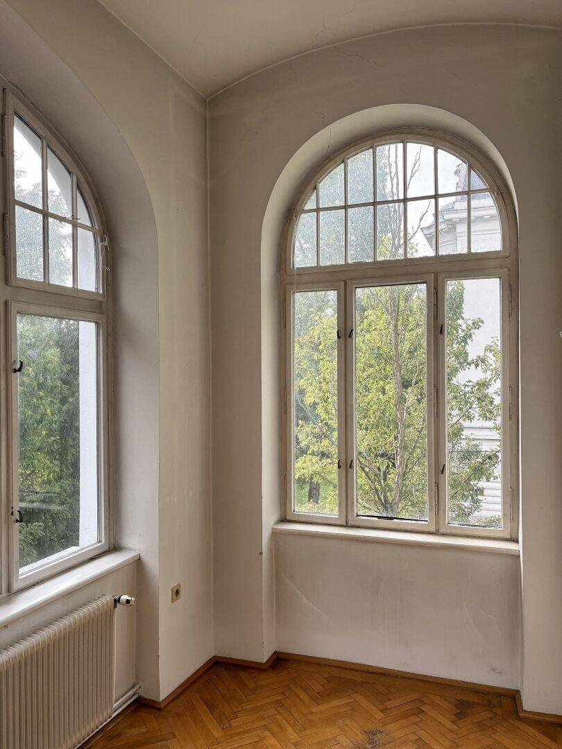 Hohe Rundbogenfenster mit Sprossen und Blick ins Grüne, die viel Tageslicht hereinlassen.