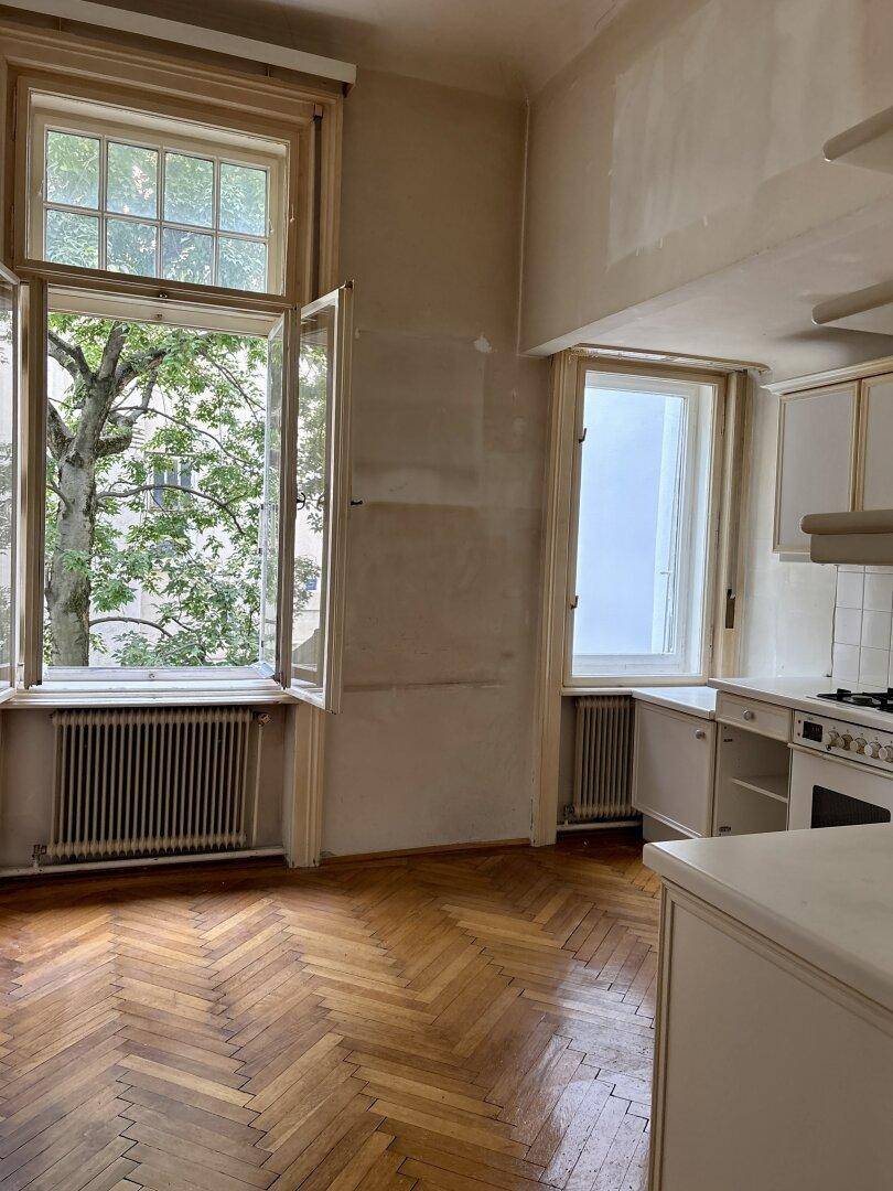 Küche mit Fischgrätparkett, großen Fenstern und Blick ins Grüne, bereit zur Modernisierung.