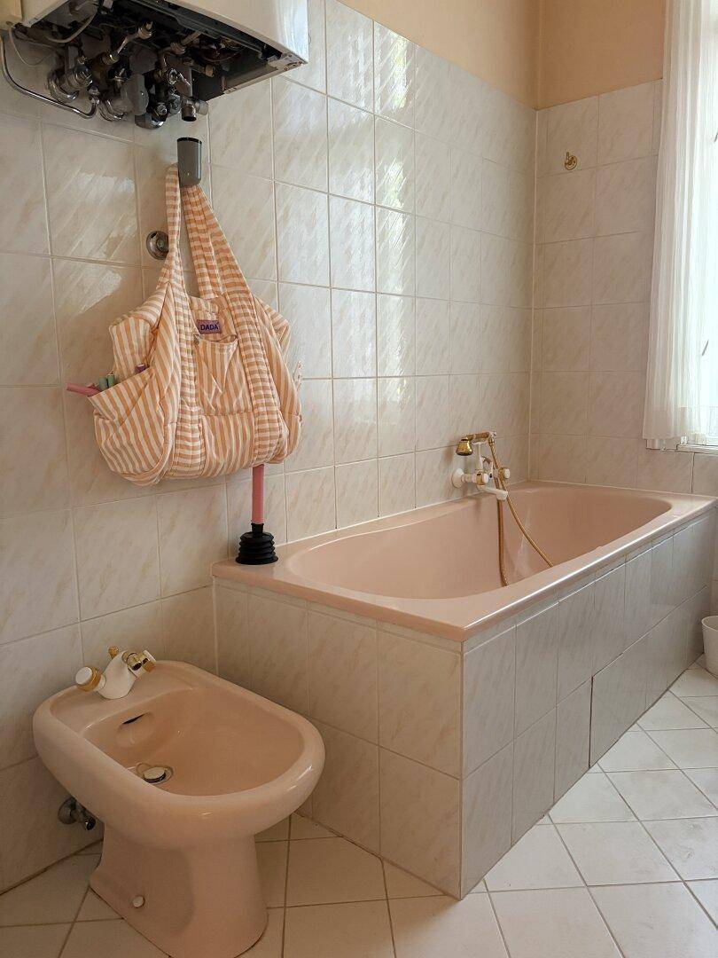 Badezimmer mit rosa Badewanne, Bidet und hellen Wandfliesen im 80er-Jahre-Stil.