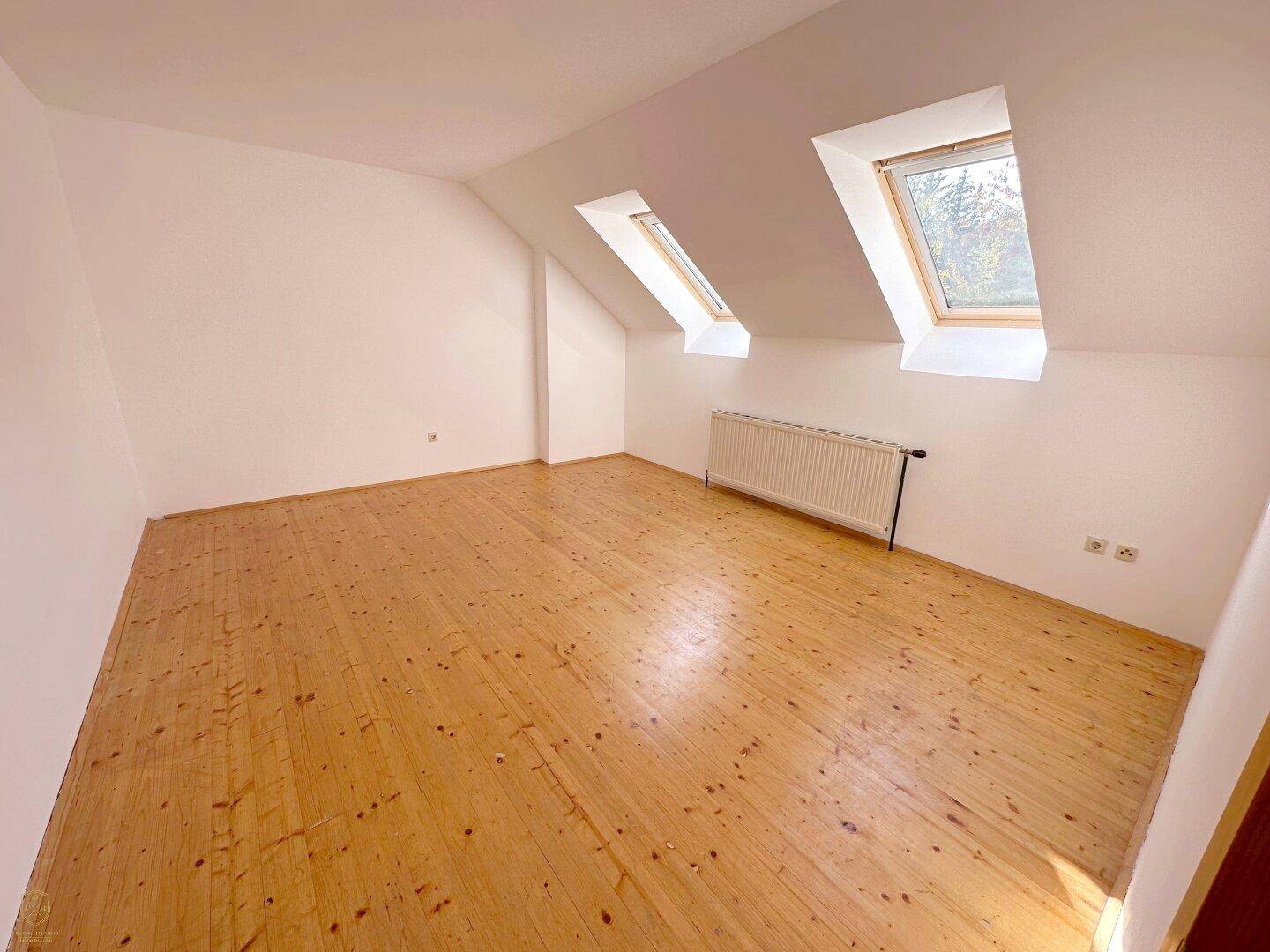Schlafzimmer im Dachgeschoss mit Holzdielenboden, Dachschrägen und zwei Dachfenstern.