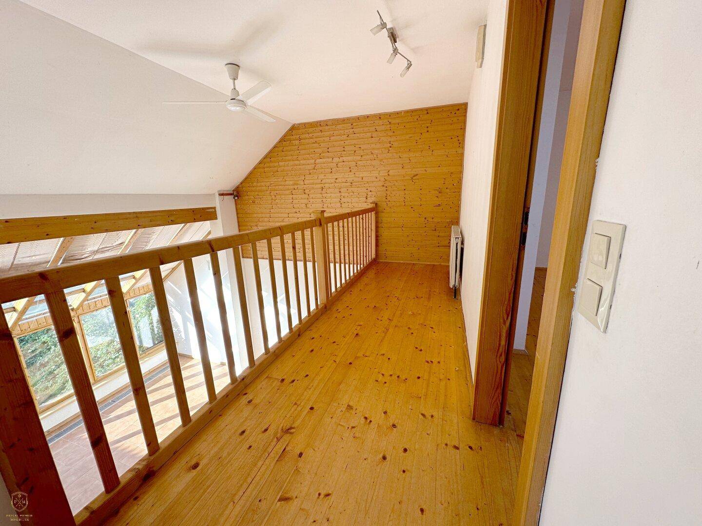 Galeriebereich im Obergeschoss mit Holzdielenboden, Holzgeländer und Deckenventilator.