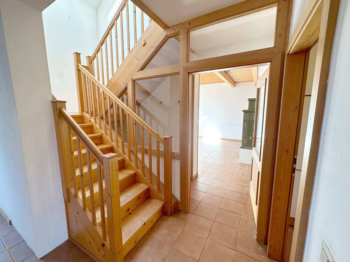 Heller Eingangsbereich mit massiver Holztreppe und Fliesenboden.