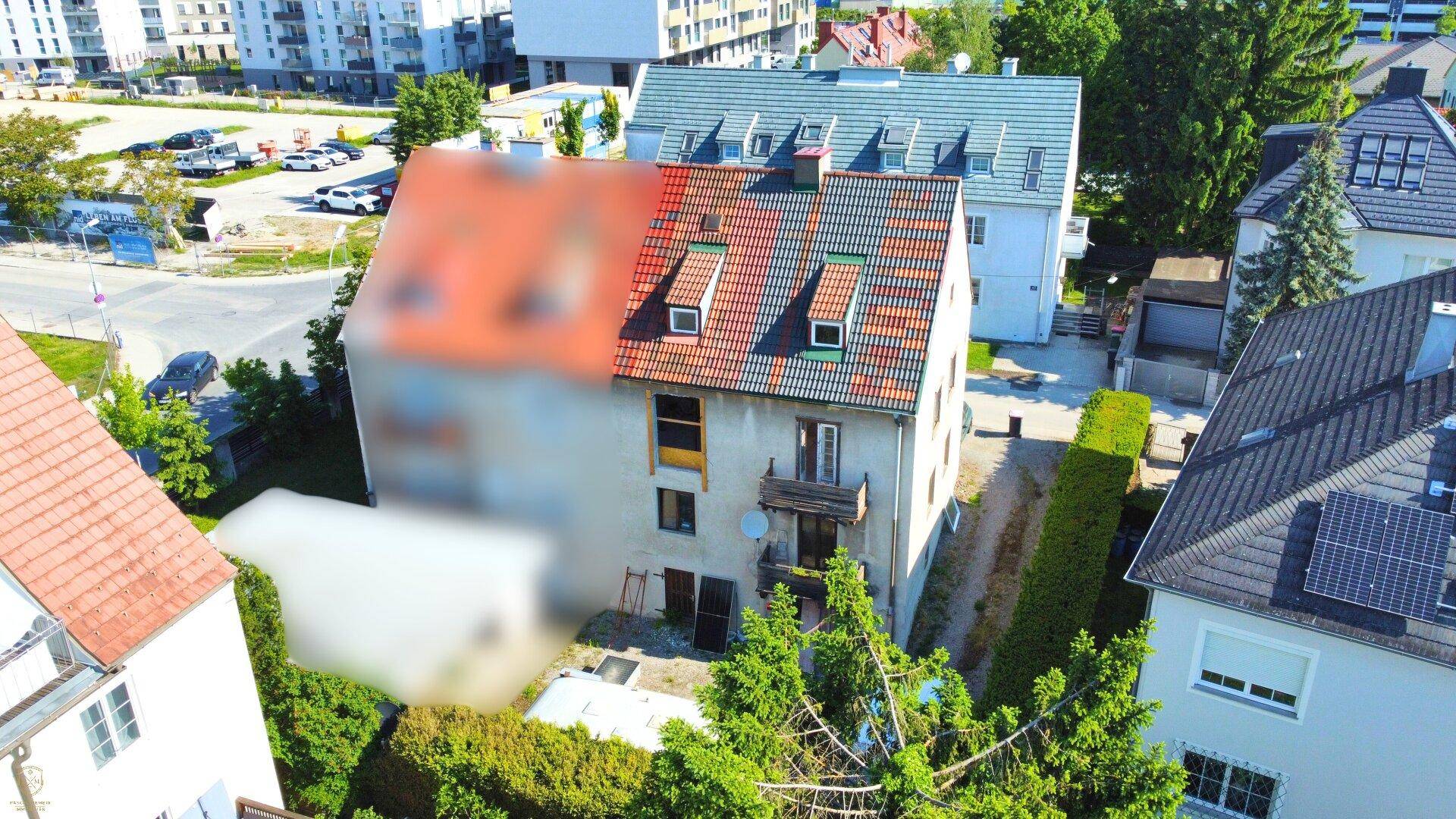 Luftaufnahme eines Wohnhauses mit Ziegeldach, Balkon und angrenzenden Gebäuden in grüner Umgebung.