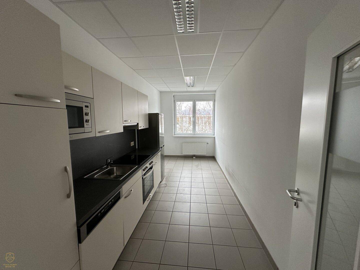 Schmale Küchenzeile mit weißen Schränken, schwarzen Arbeitsplatten und integrierten Geräten, ideal für ein Büro.