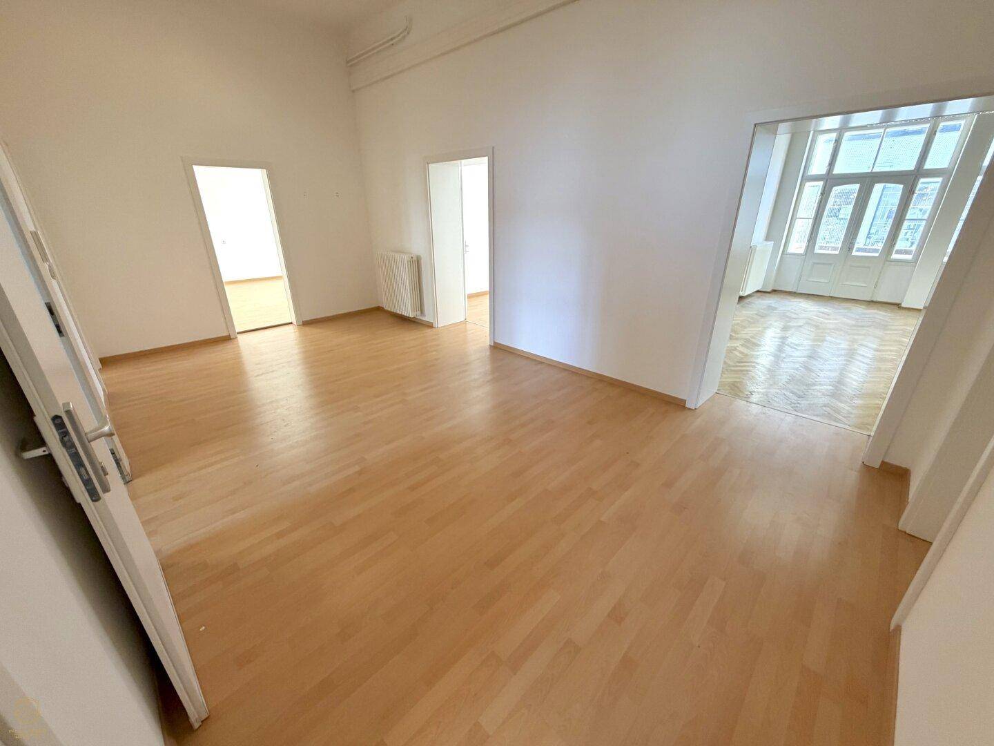 Heller, leerer Raum mit Laminatboden und mehreren Türen, die zu weiteren Zimmern führen.